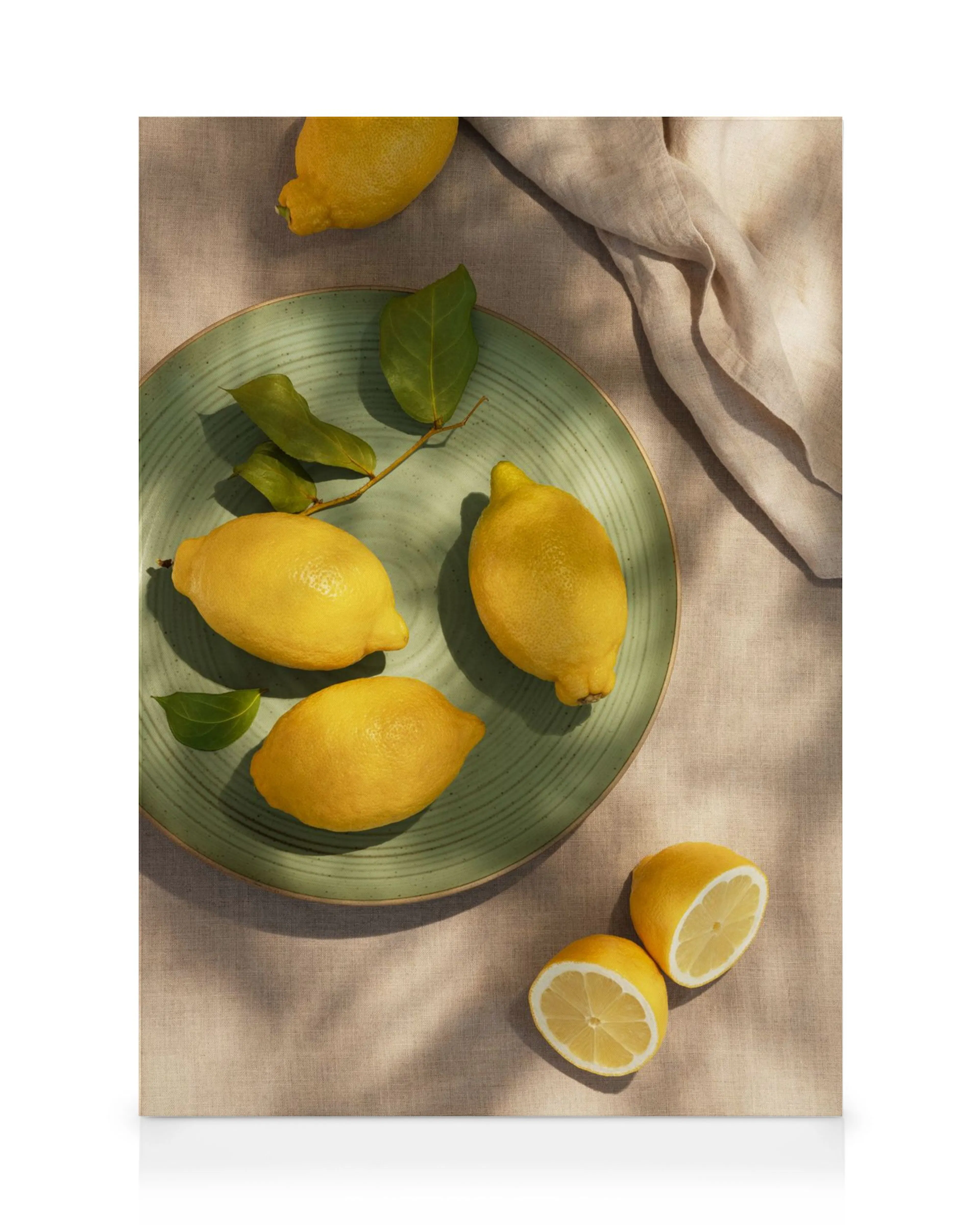Lienzo de limones amarillos frescos, algunos en un plato verde y otros cortados por la mitad, sobre tela clara.