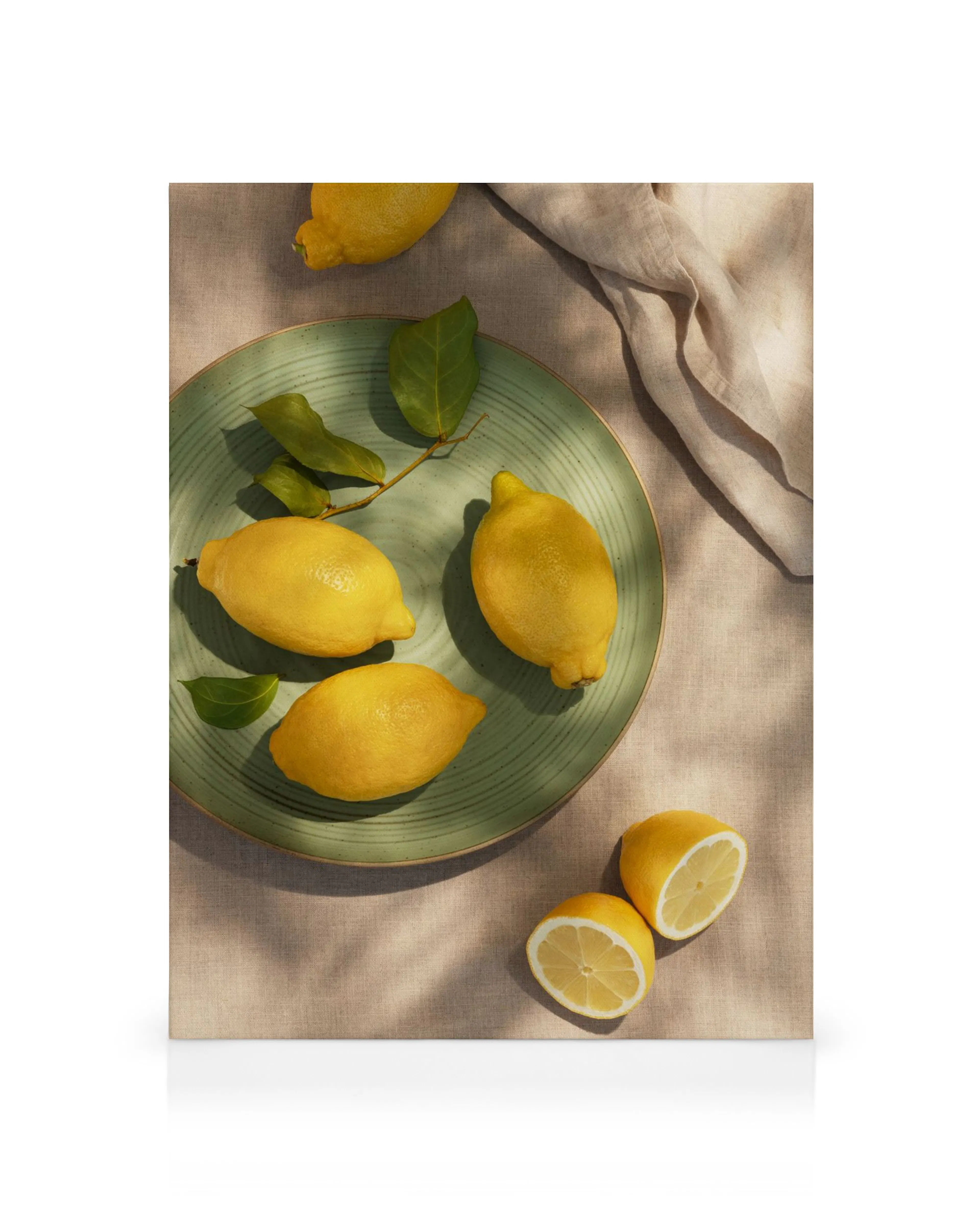 Toile de citrons jaunes frais sur une assiette verte, avec quelques feuilles et un citron coupé sur un tissu beige.