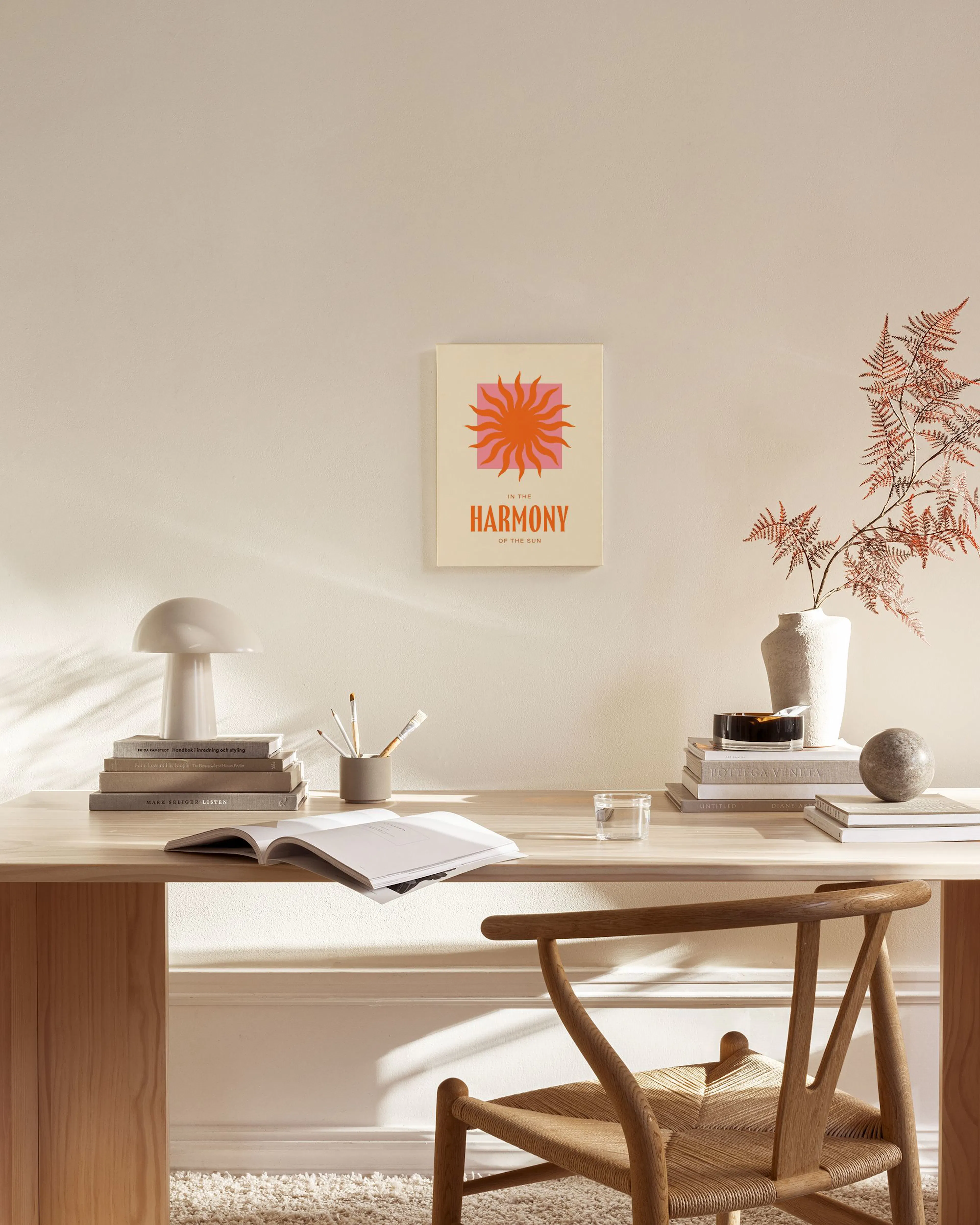 A canvas print with an orange sun over a pink square on a cream background, text below reads IN THE HARMONY OF THE SUN.