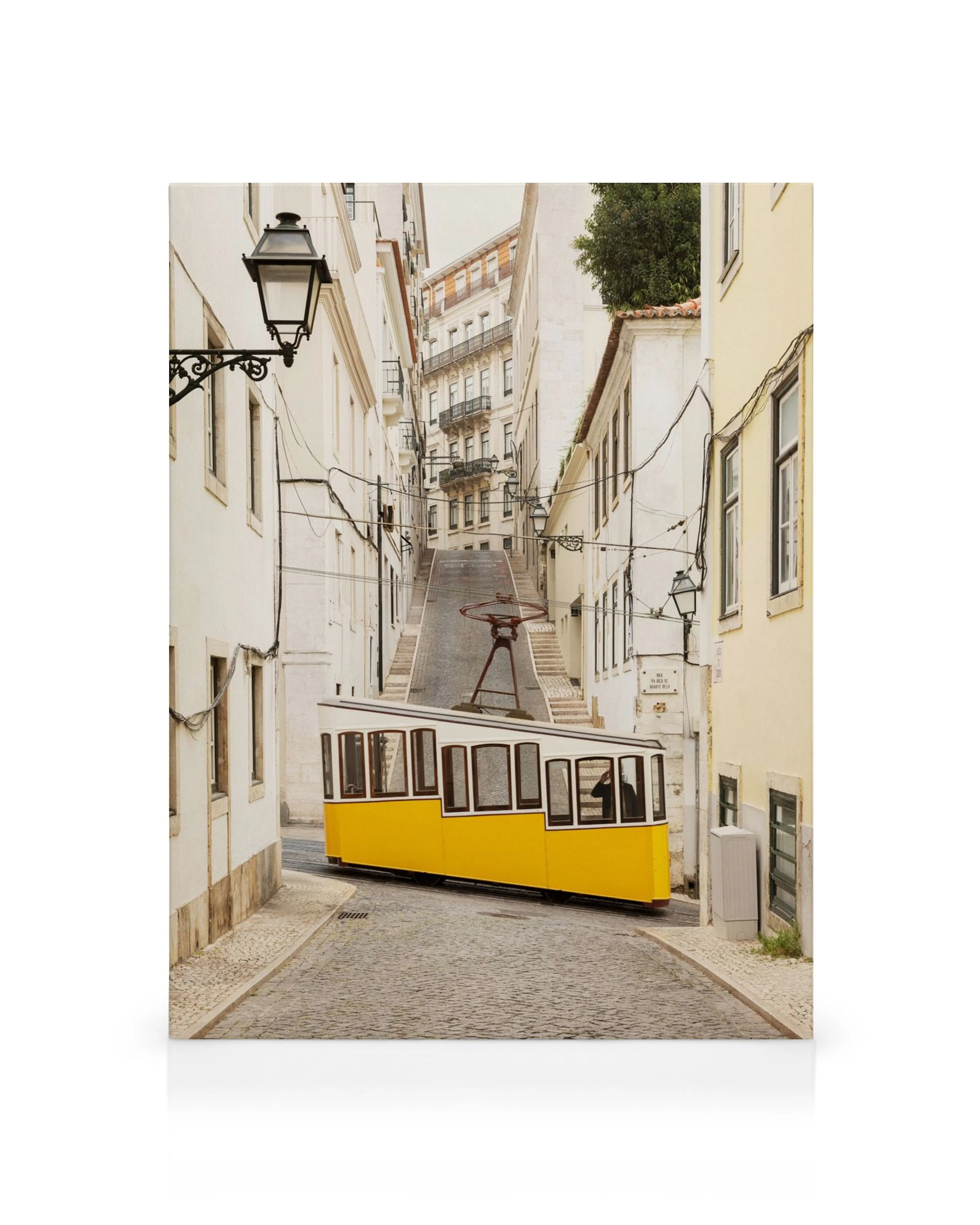 A canvas print featuring a yellow tram on a cobblestone street, surrounded by tall white and cream buildings.