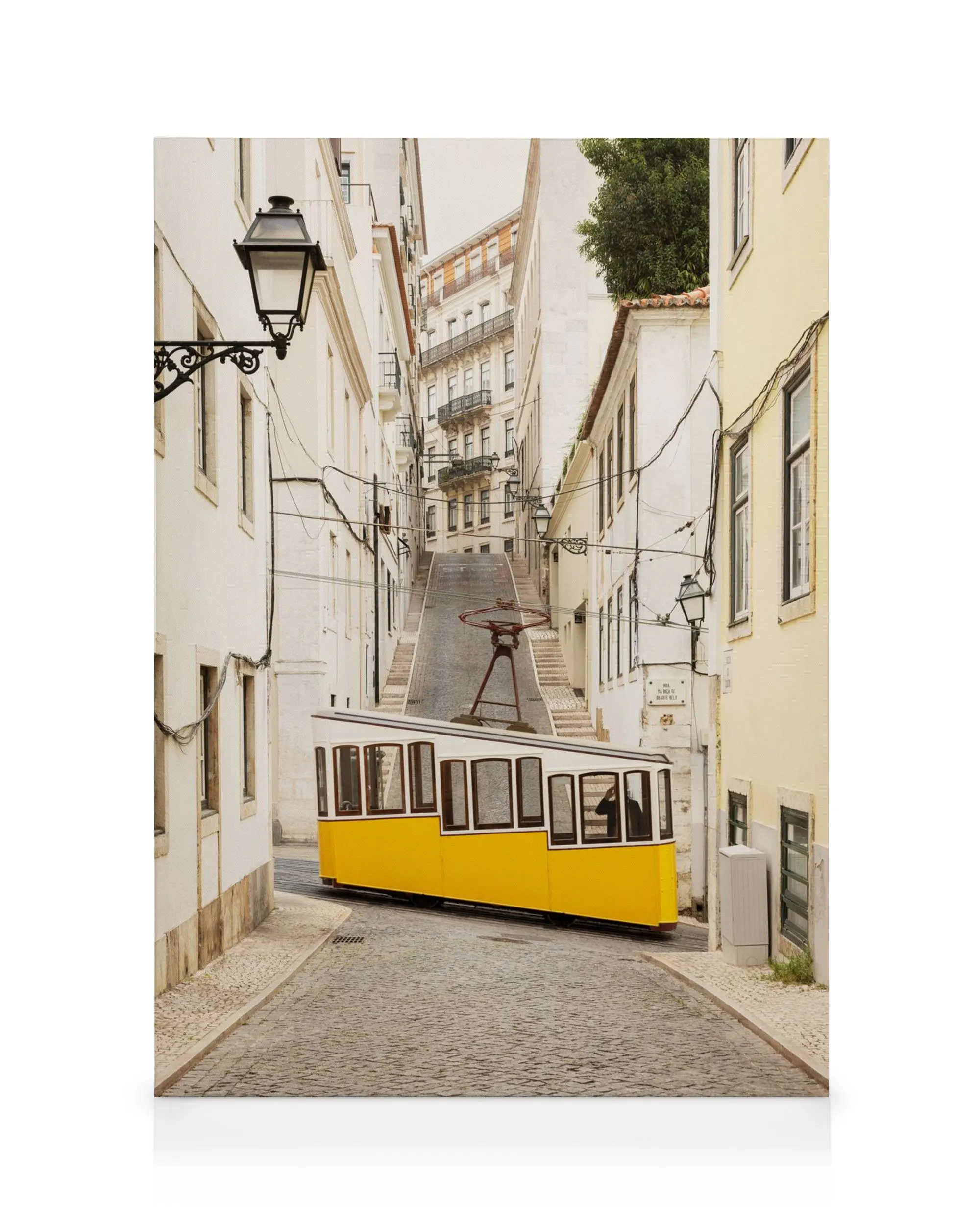 A canvas print of a bright yellow tram on a cobbled street in Lisbon, with white buildings lining the steep hill.