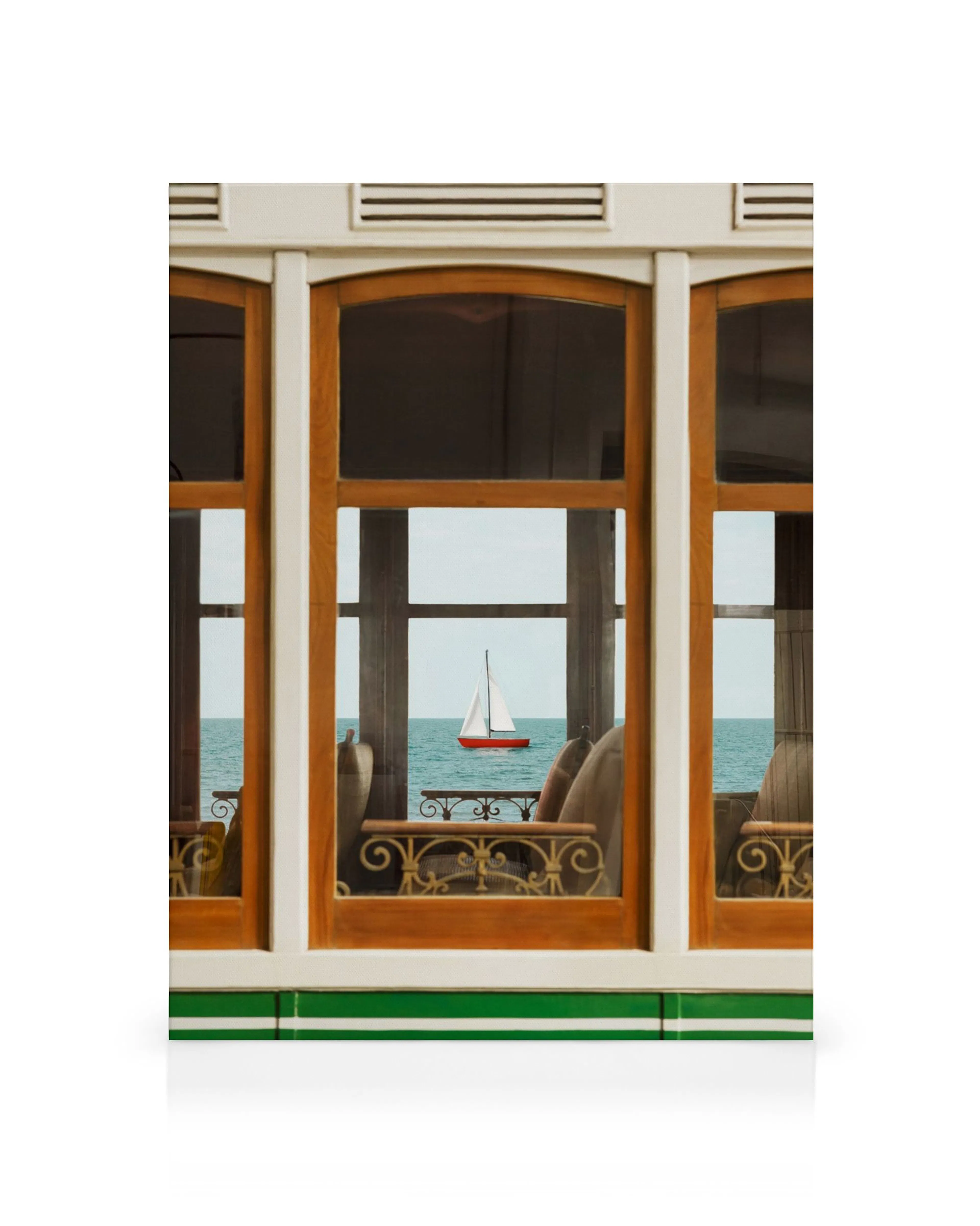 A canvas print showing a sailboat with a red hull on the blue sea, viewed through a white and wooden window frame.