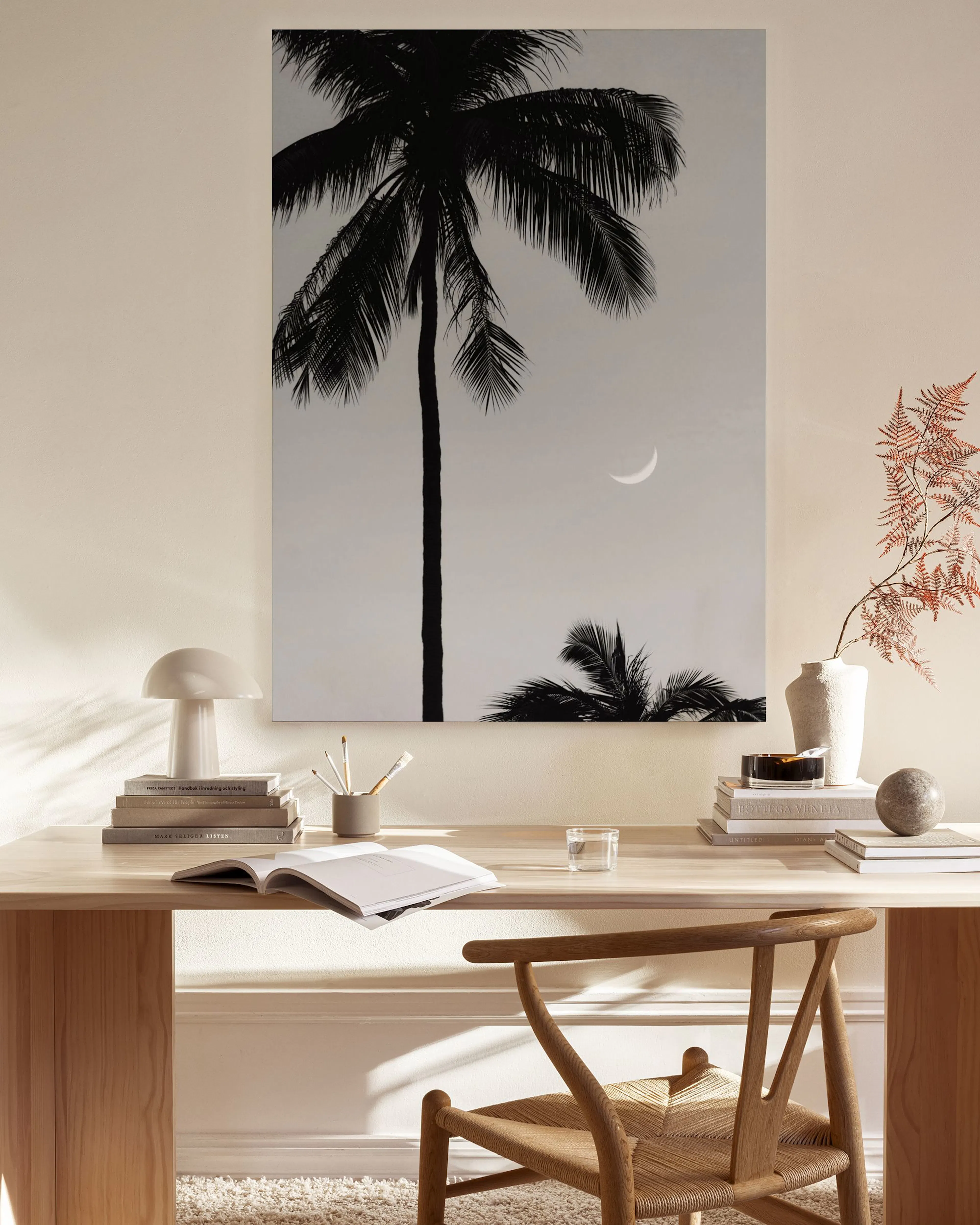 A black and white canvas print of a palm tree and crescent moon, hanging in a neutral-toned living room.