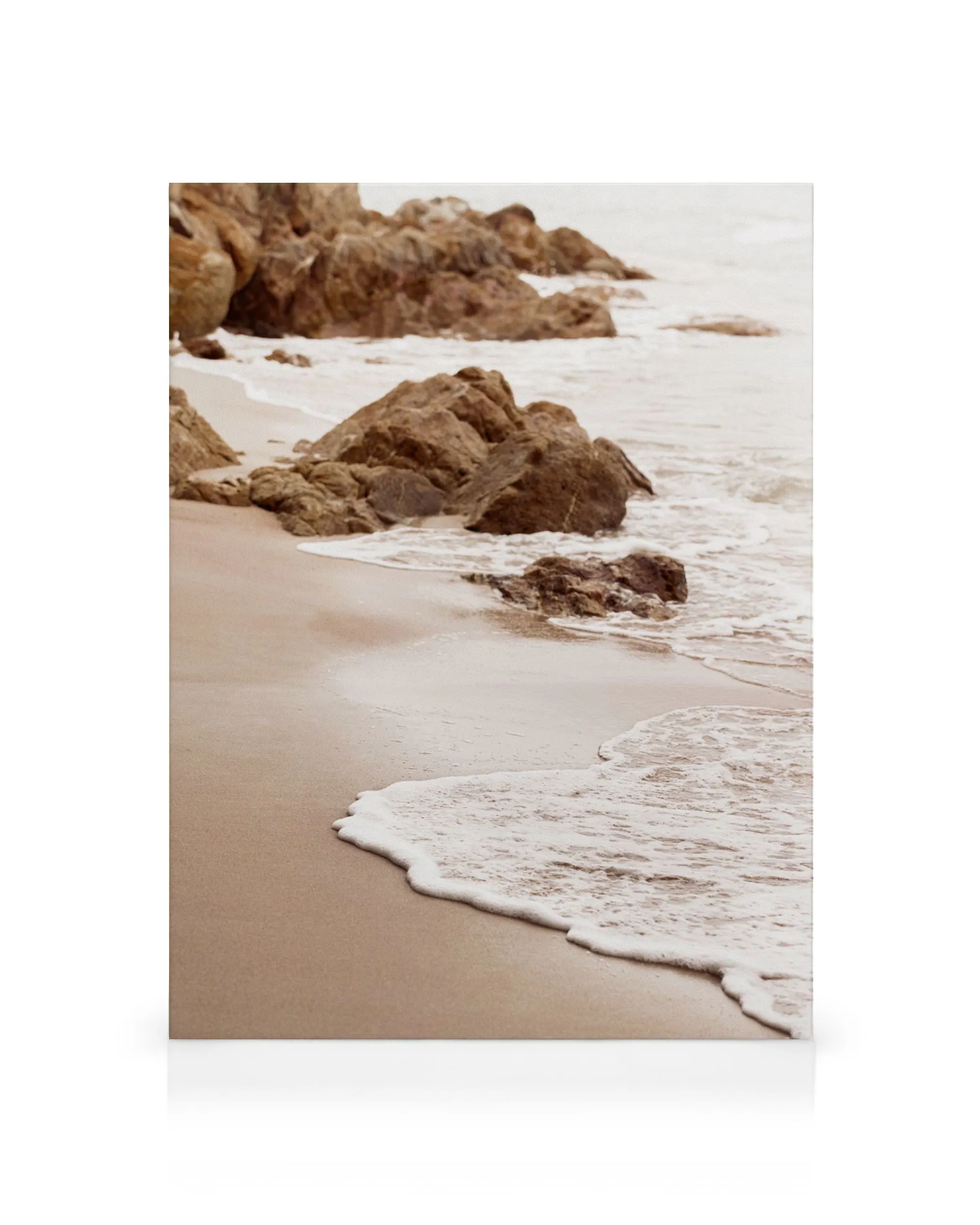 A serene beach scene canvas print with waves gently lapping at the sand, and rocky outcrops in the background.