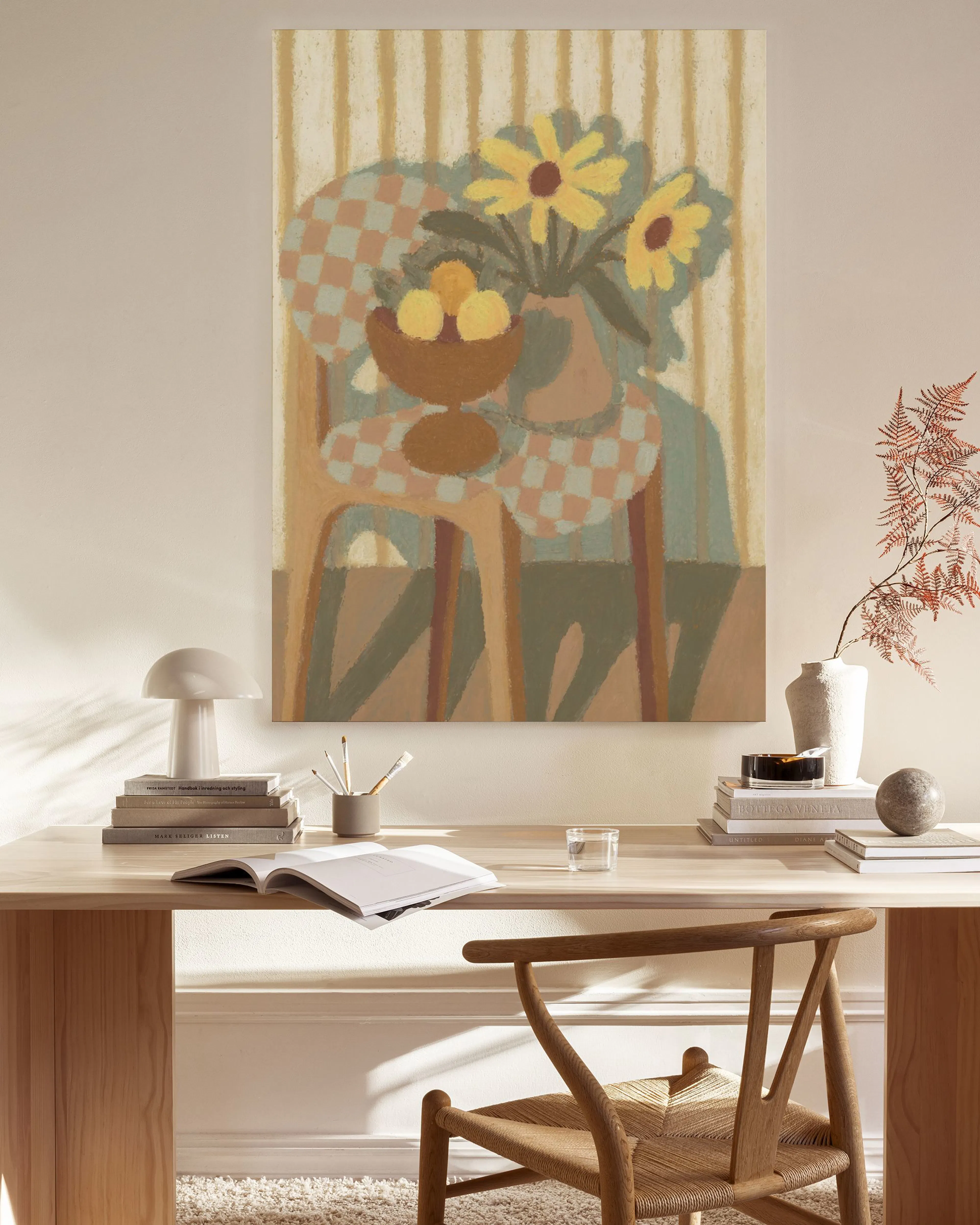 A colorful still life print with yellow flowers and fruit on a checkered tablecloth, hanging above a console table in a neutral-