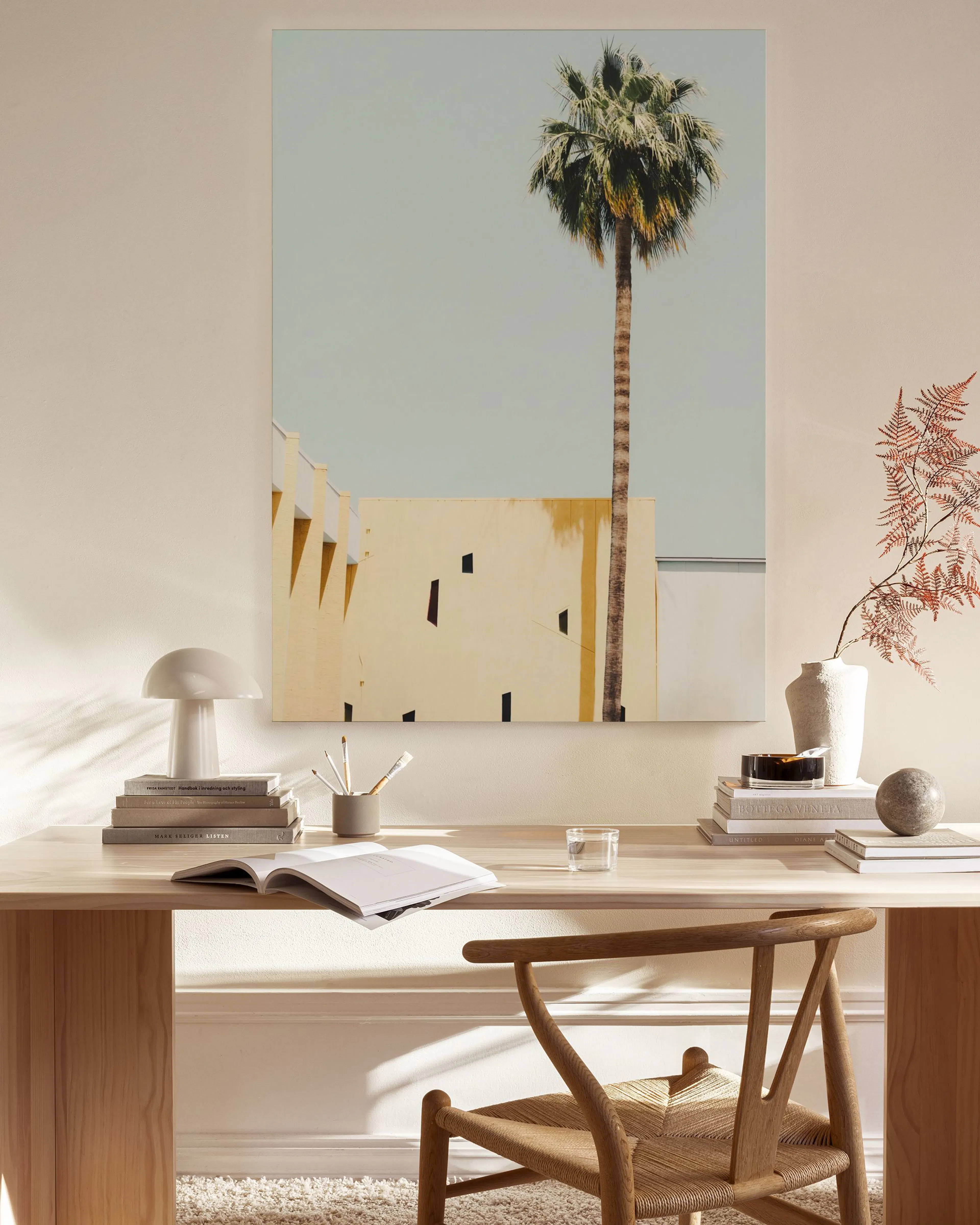 Lienzo de una palmera solitaria contra un edificio ocre y cielo azul claro, colgado en una sala de estar minimalista.