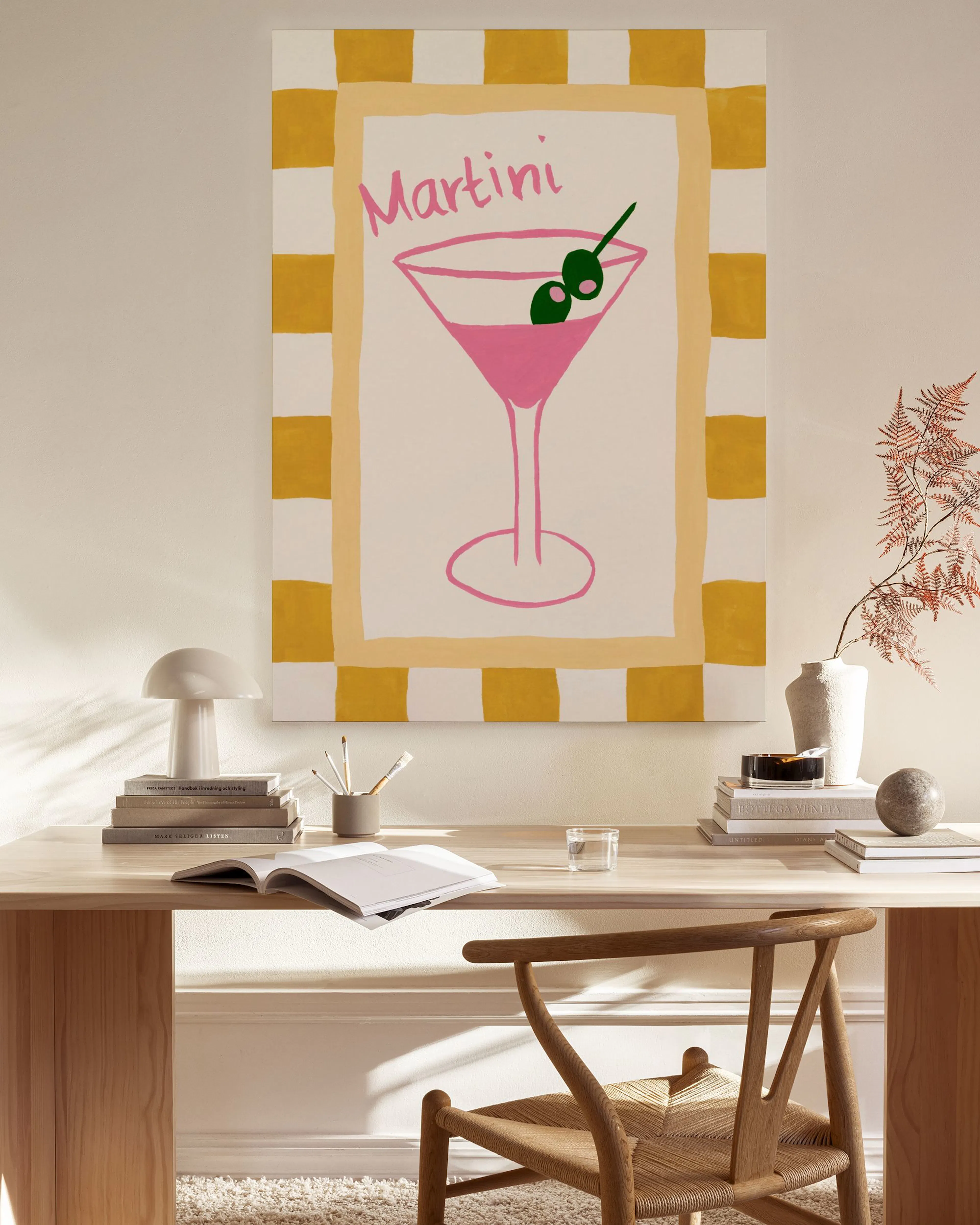 Stampa su tela di un bicchiere di Martini rosa con olive, su sfondo a scacchi gialli, appesa in un soggiorno moderno.