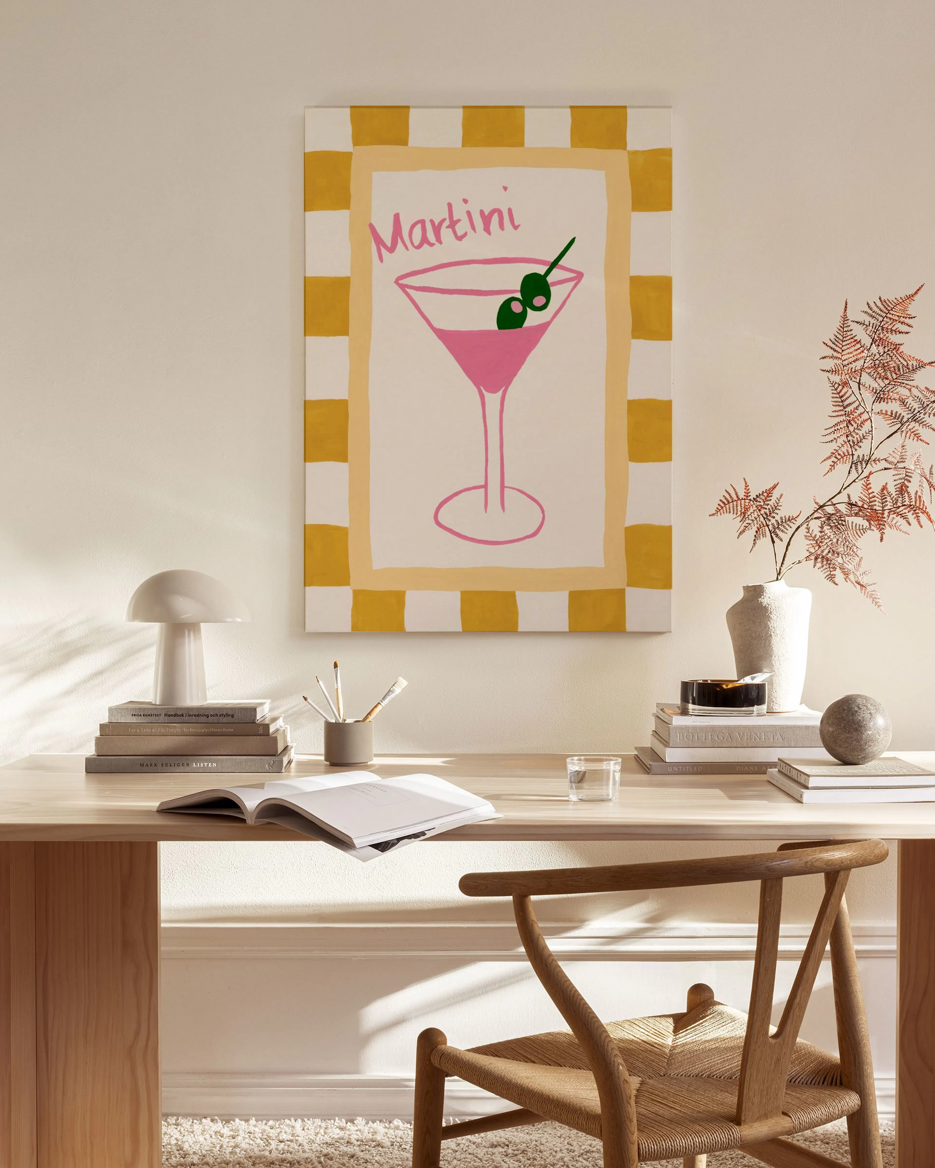 A vibrant martini glass canvas print with pink liquid and olives on a checkered background, hanging in a bright living room.