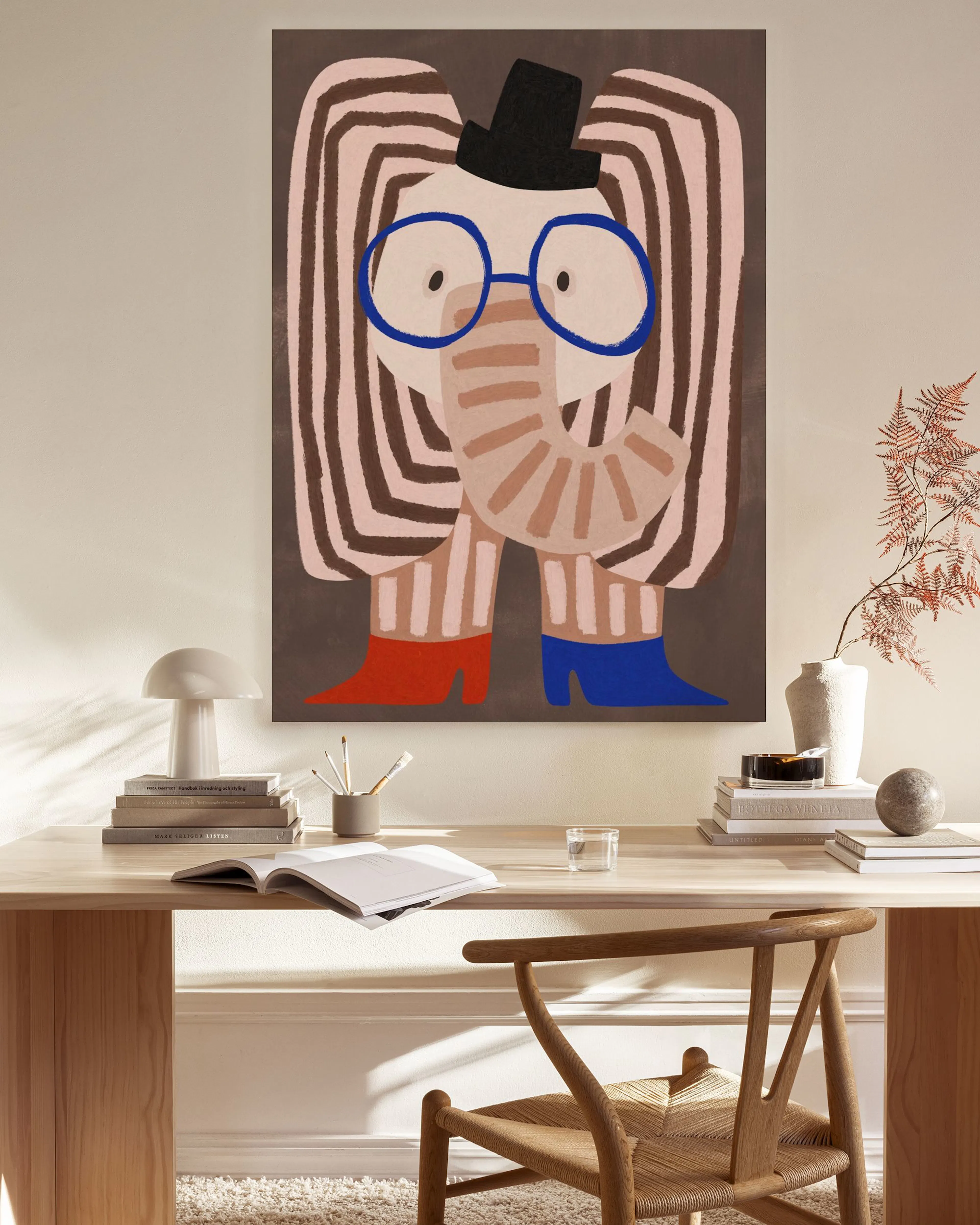 Leinwandbild mit einem abstrakten Gesicht mit Hut, blauer Brille und gestreiften Armen, das in einem hellen Wohnzimmer über eine