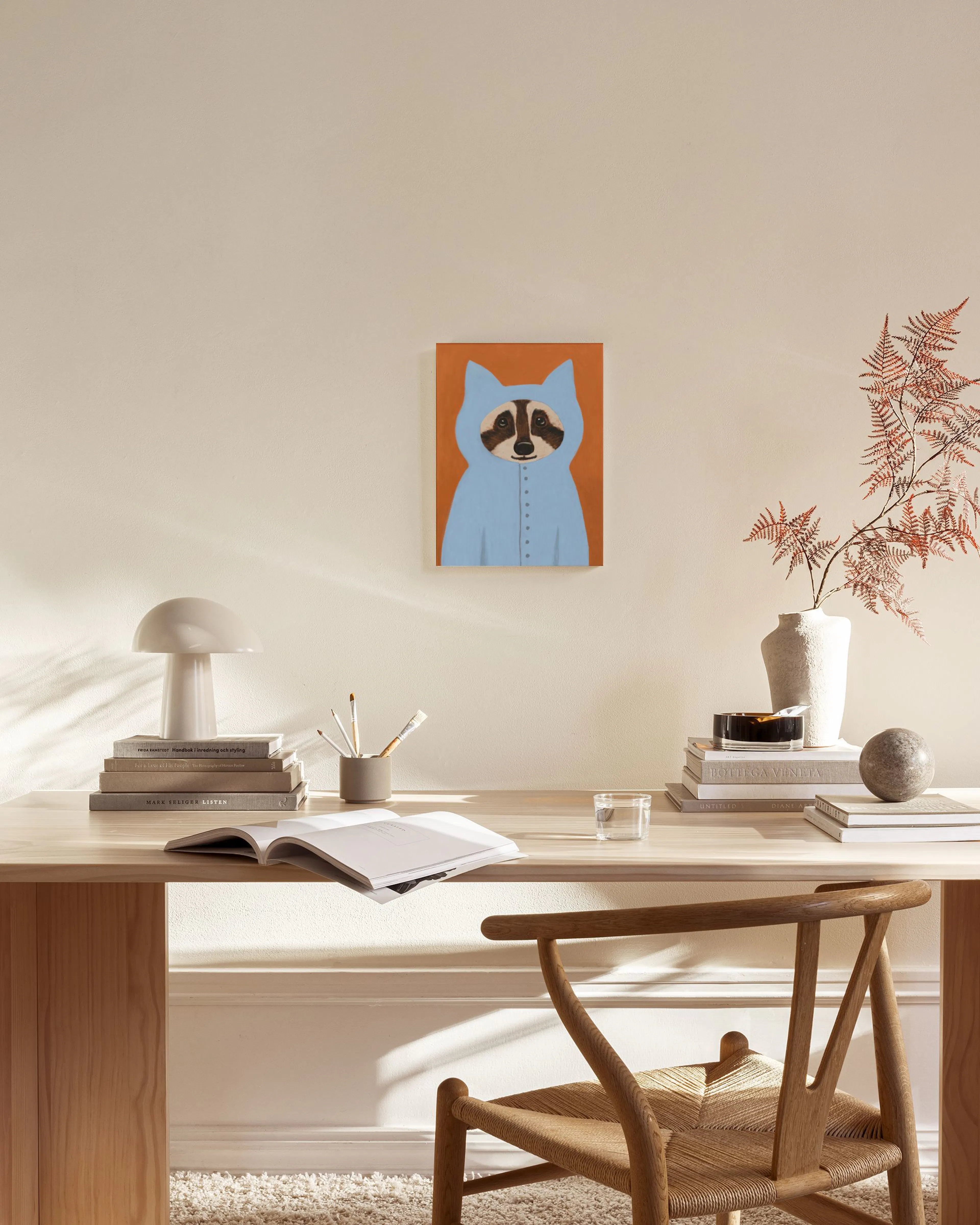 Lienzo de un mapache con capucha azul sobre fondo naranja, colgado en una sala de estar moderna con muebles de madera clara.