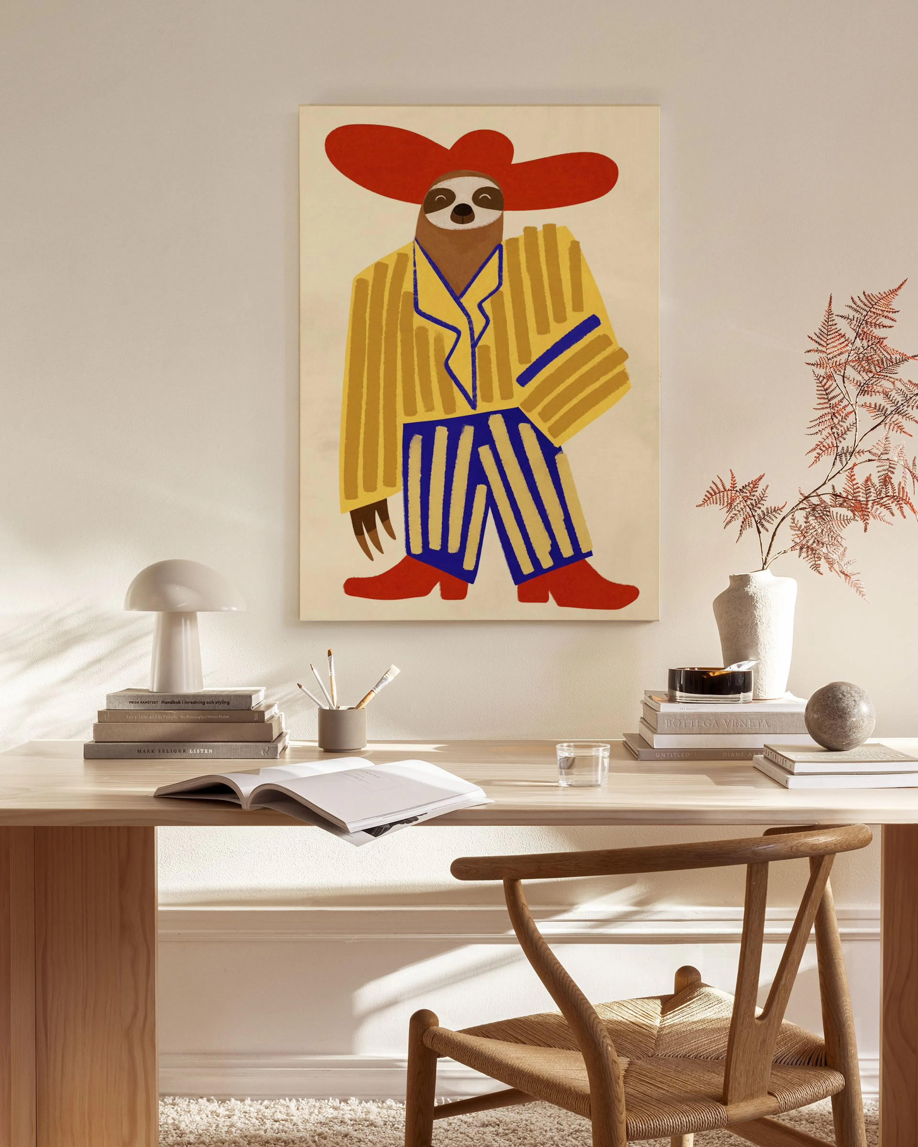 A canvas print of a sloth in yellow and blue striped pajamas with a red hat, hanging in a bright living room.