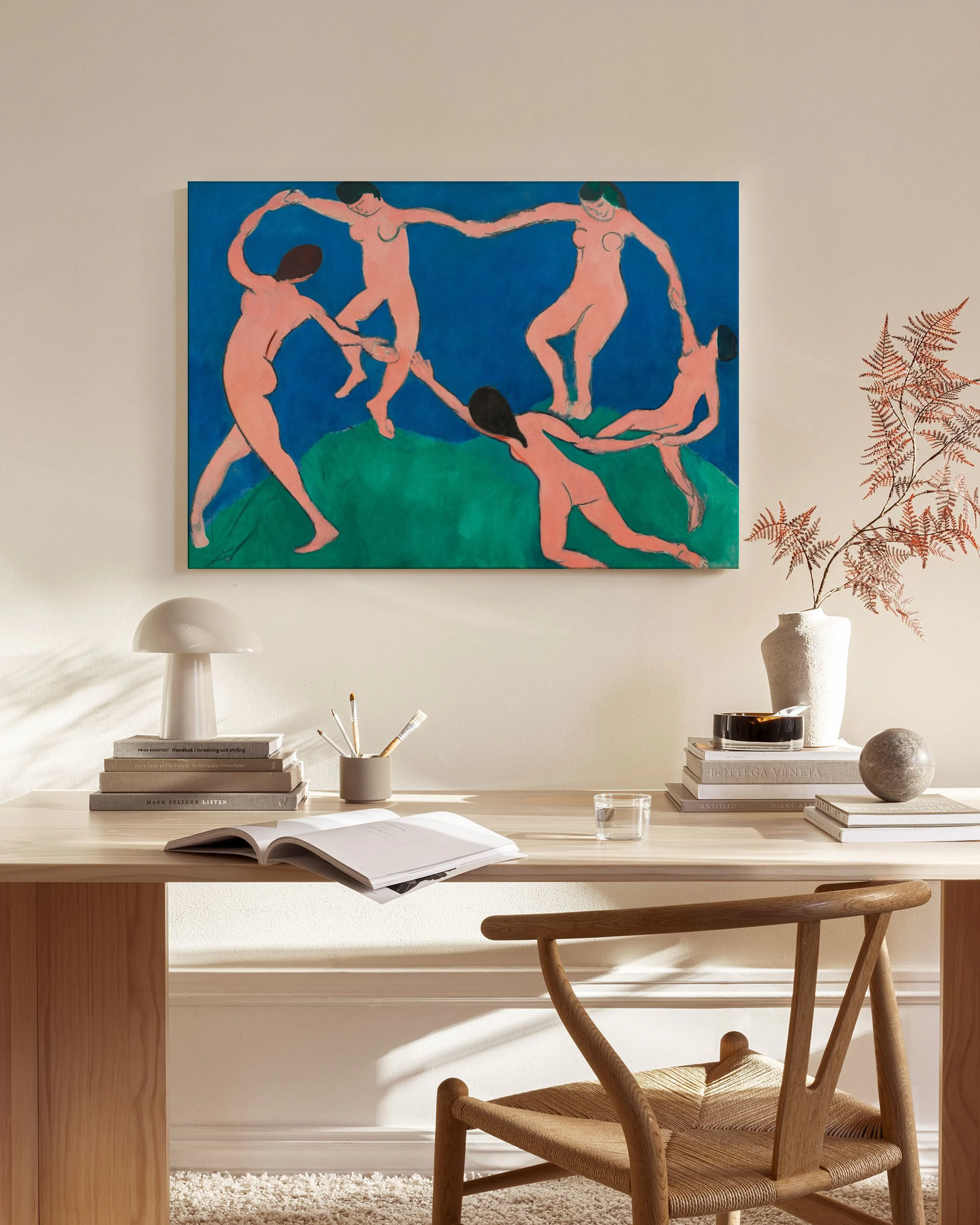 A canvas print of five nude figures dancing in a circle on blue and green, displayed in a living room above a wooden console.