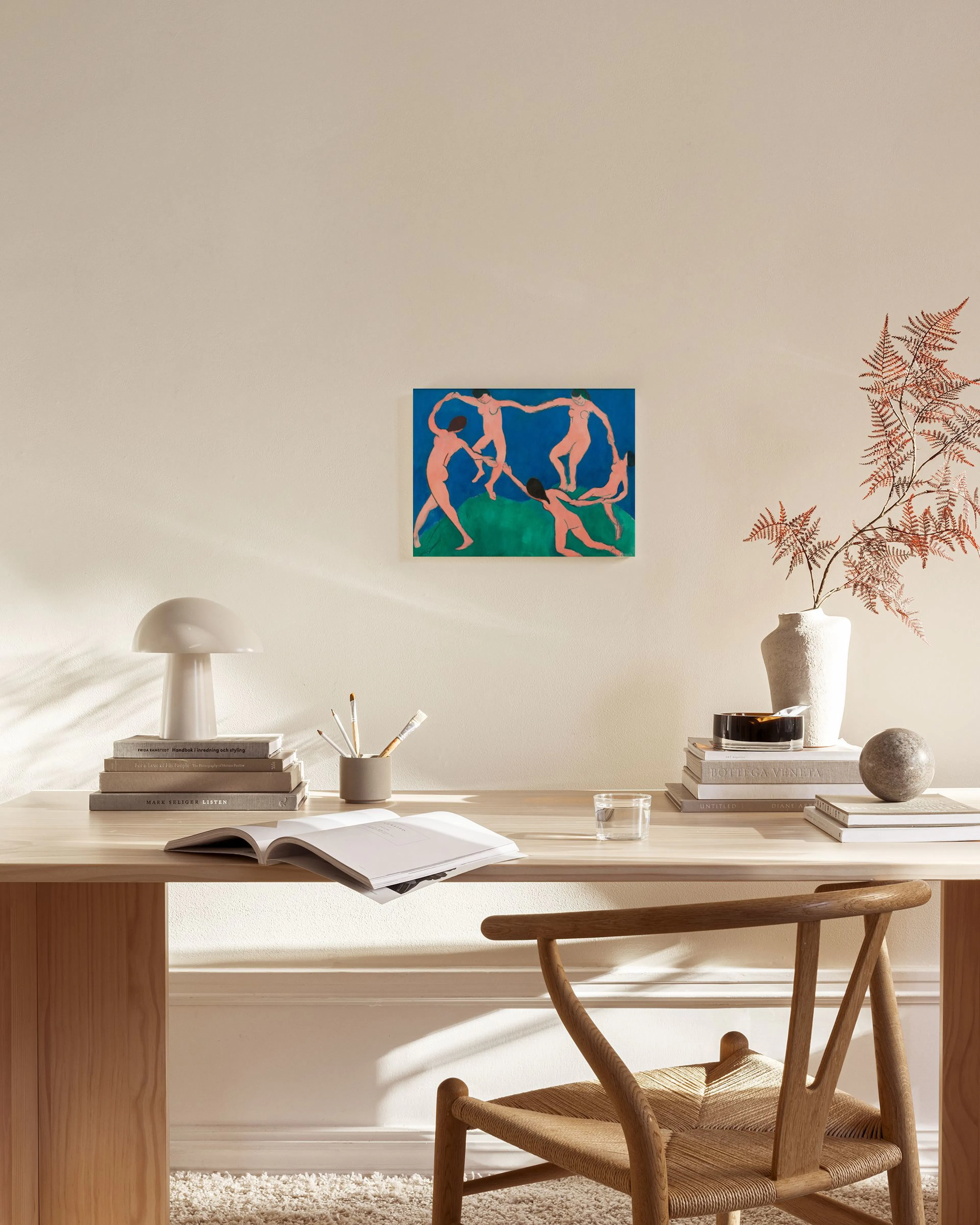 Tela decorativa com pintura de figuras humanas em dança, tons de rosa e azul, exibida numa sala de estar minimalista.