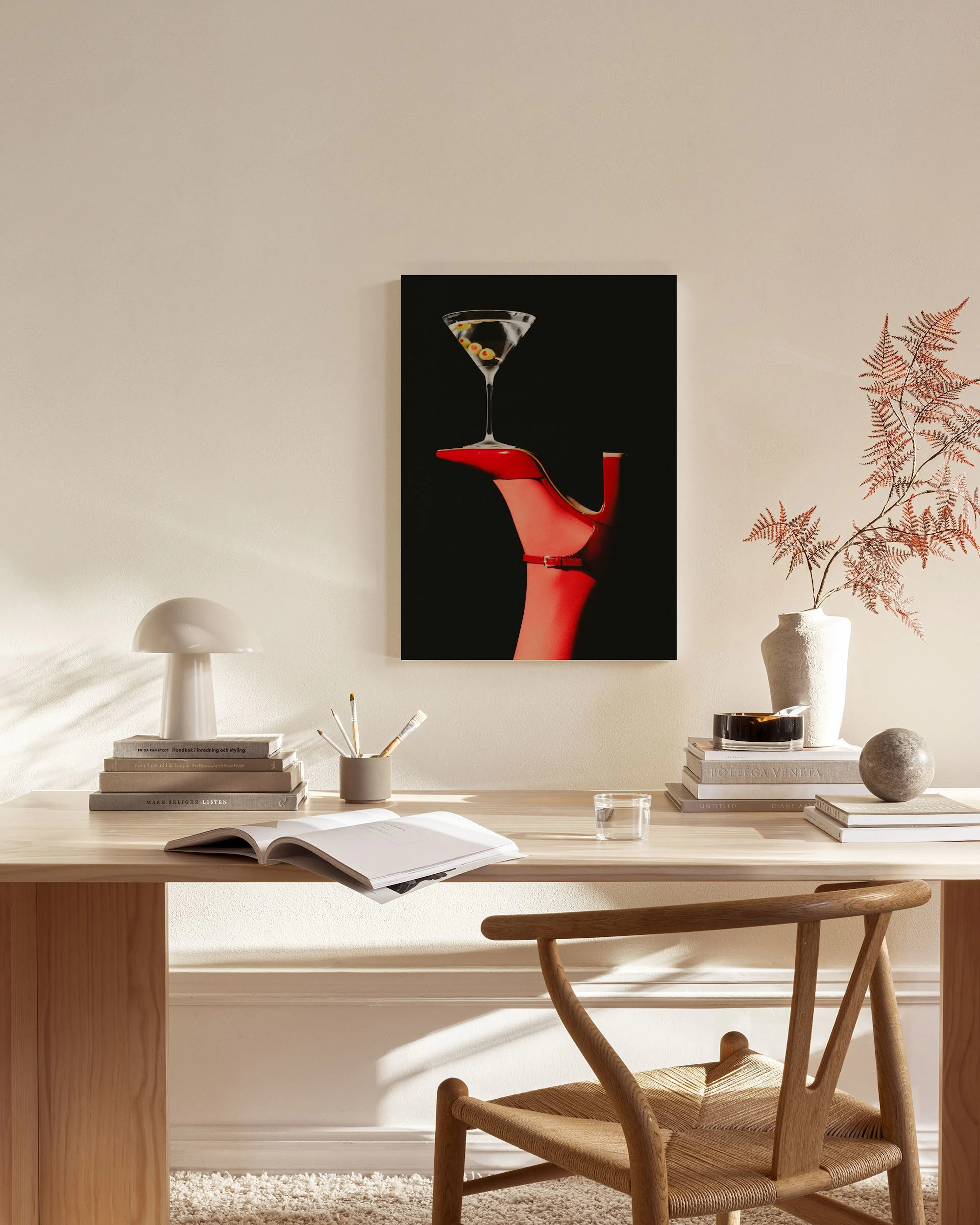 Lienzo de cóctel de martini sobre zapato de tacón rojo en fondo negro, colgado sobre un mueble bajo en una sala de estar.