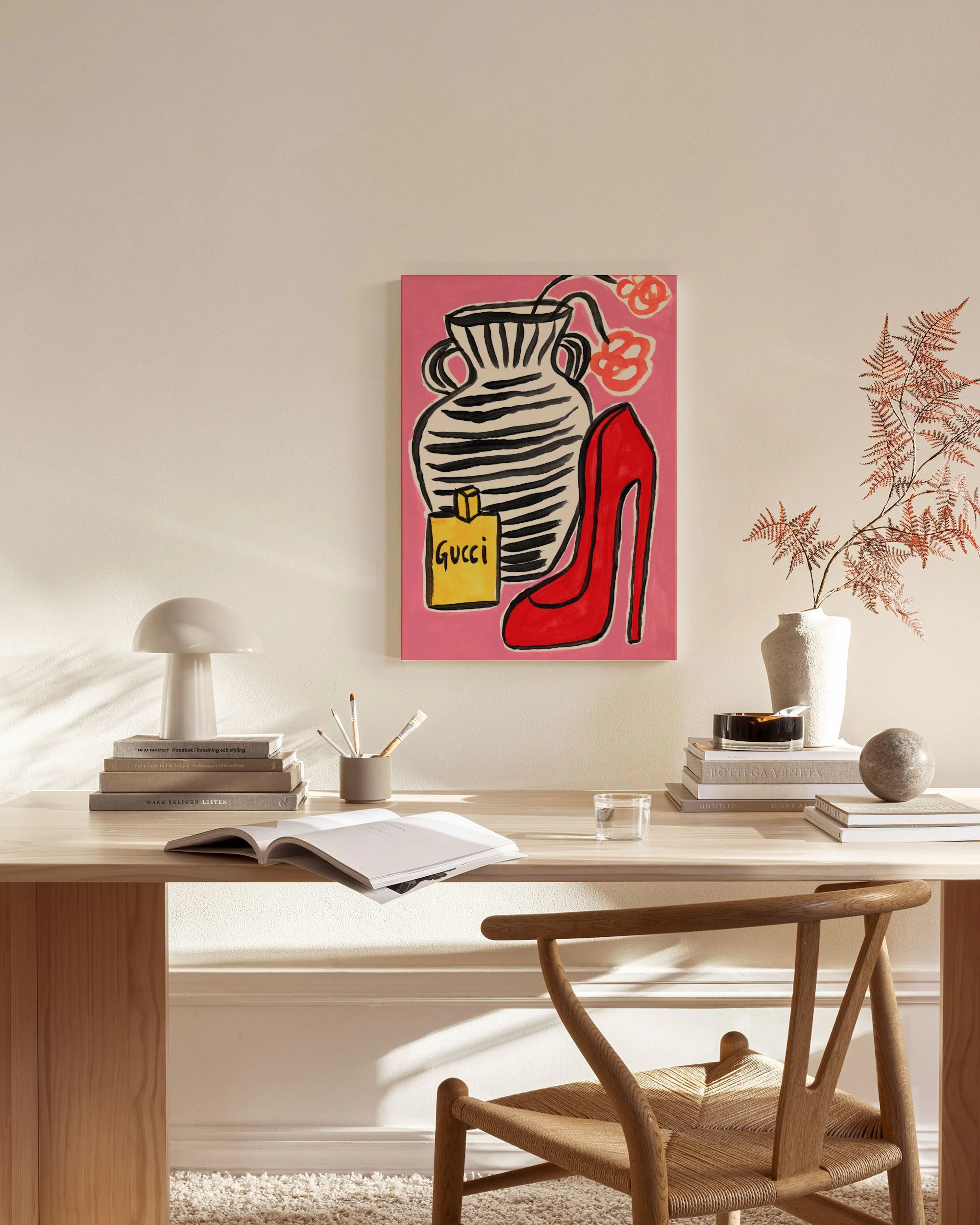 Vibrant canvas print with a red high heel, black and white striped vase, and yellow perfume bottle on a pink background, hanging