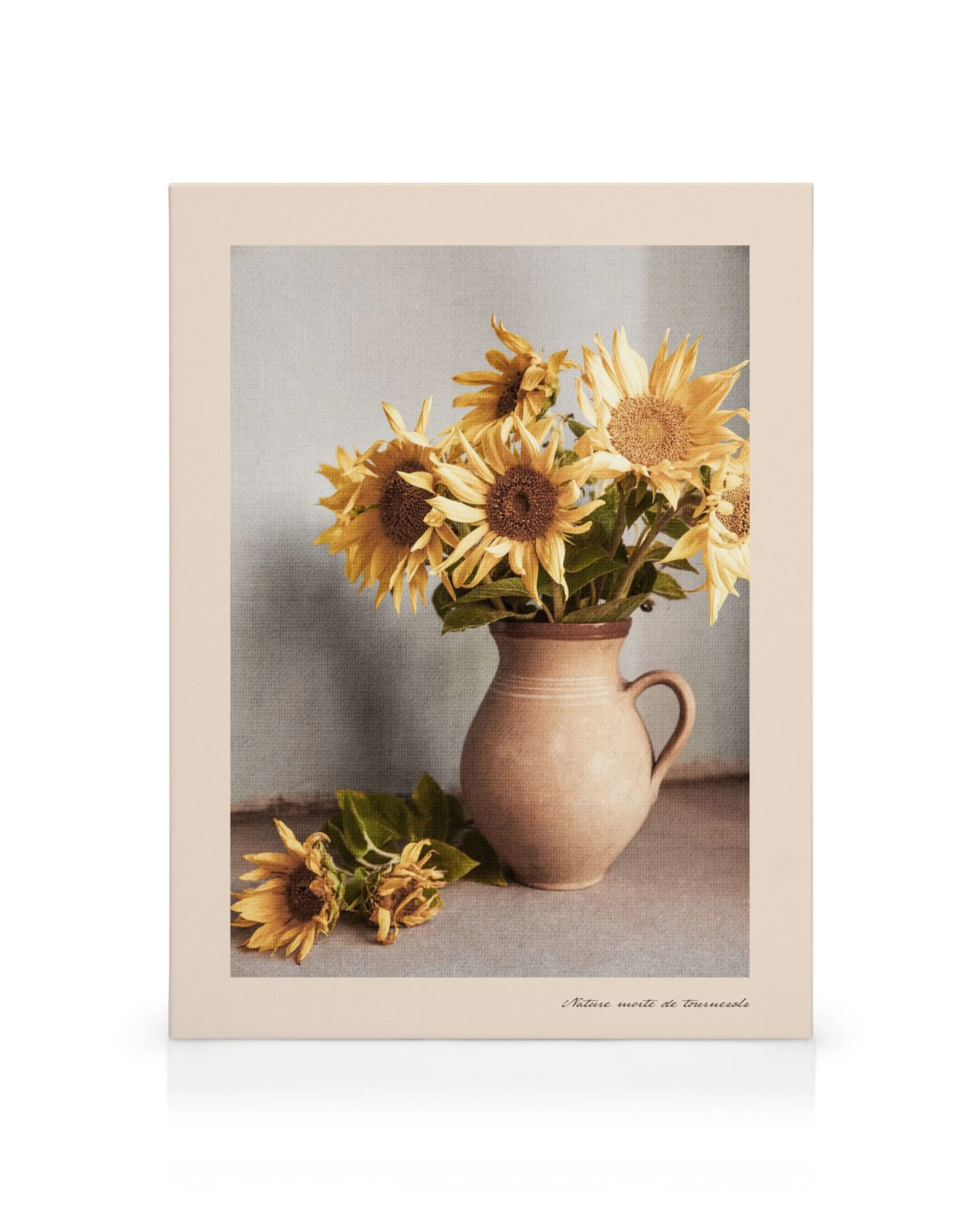Jarrón rústico con girasoles amarillos y hojas verdes sobre una superficie gris, con dos girasoles caídos.
