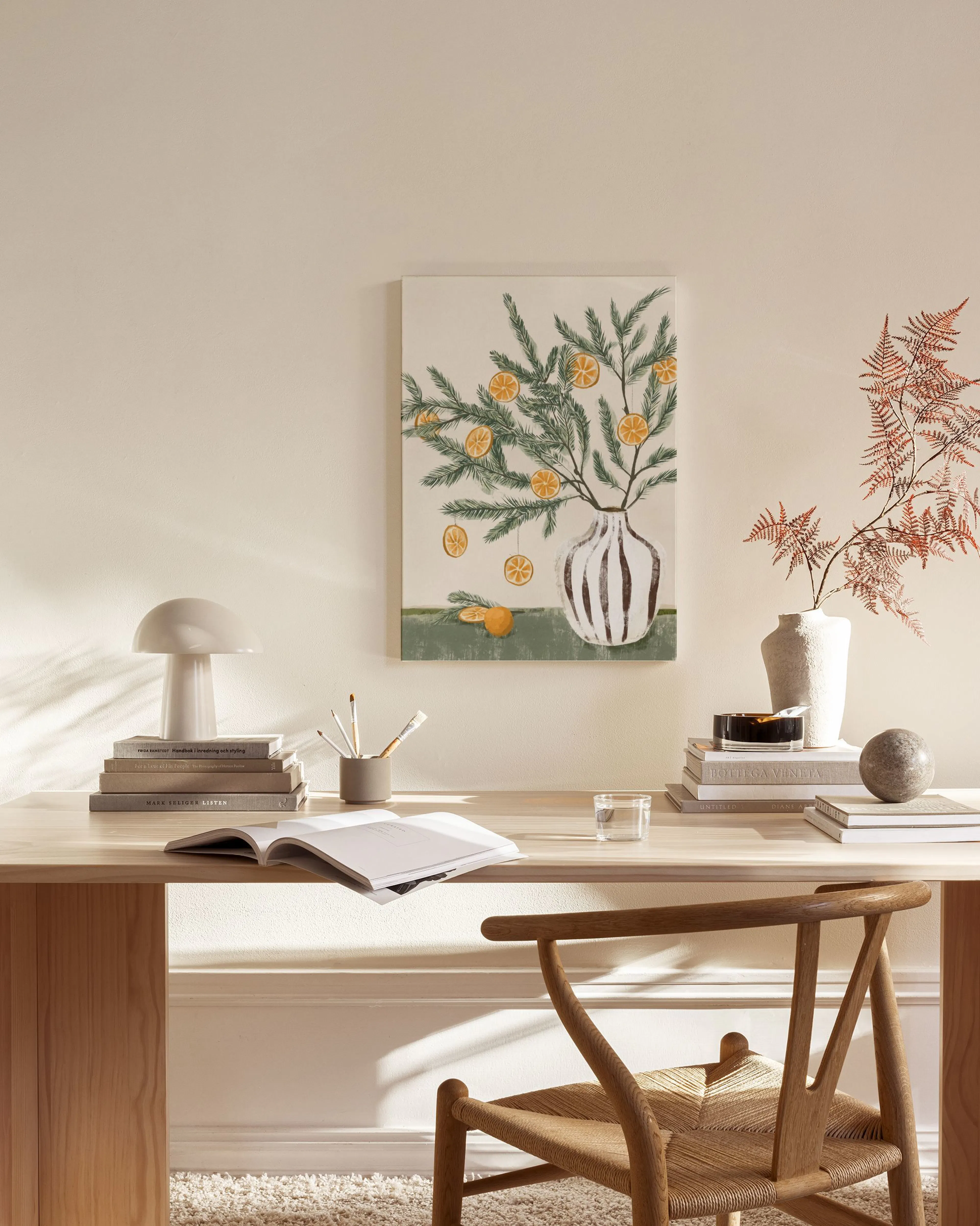A canvas print of pine branches with orange slices in a striped vase, hanging above a wooden console table in a minimalist livin