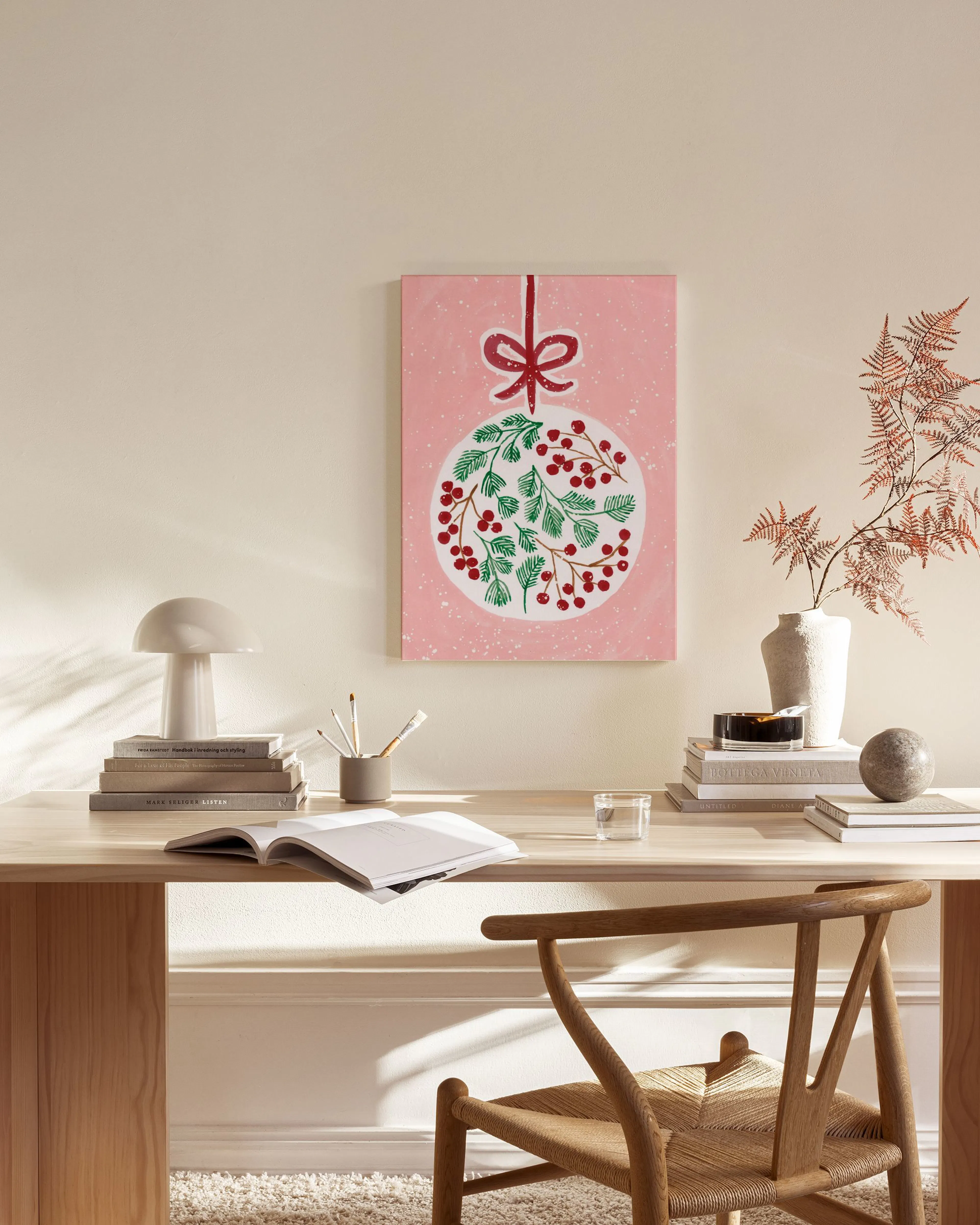 Lerretsbilde av et juleornament med bær og grønne grener på rosa bakgrunn, henger i en moderne stue.