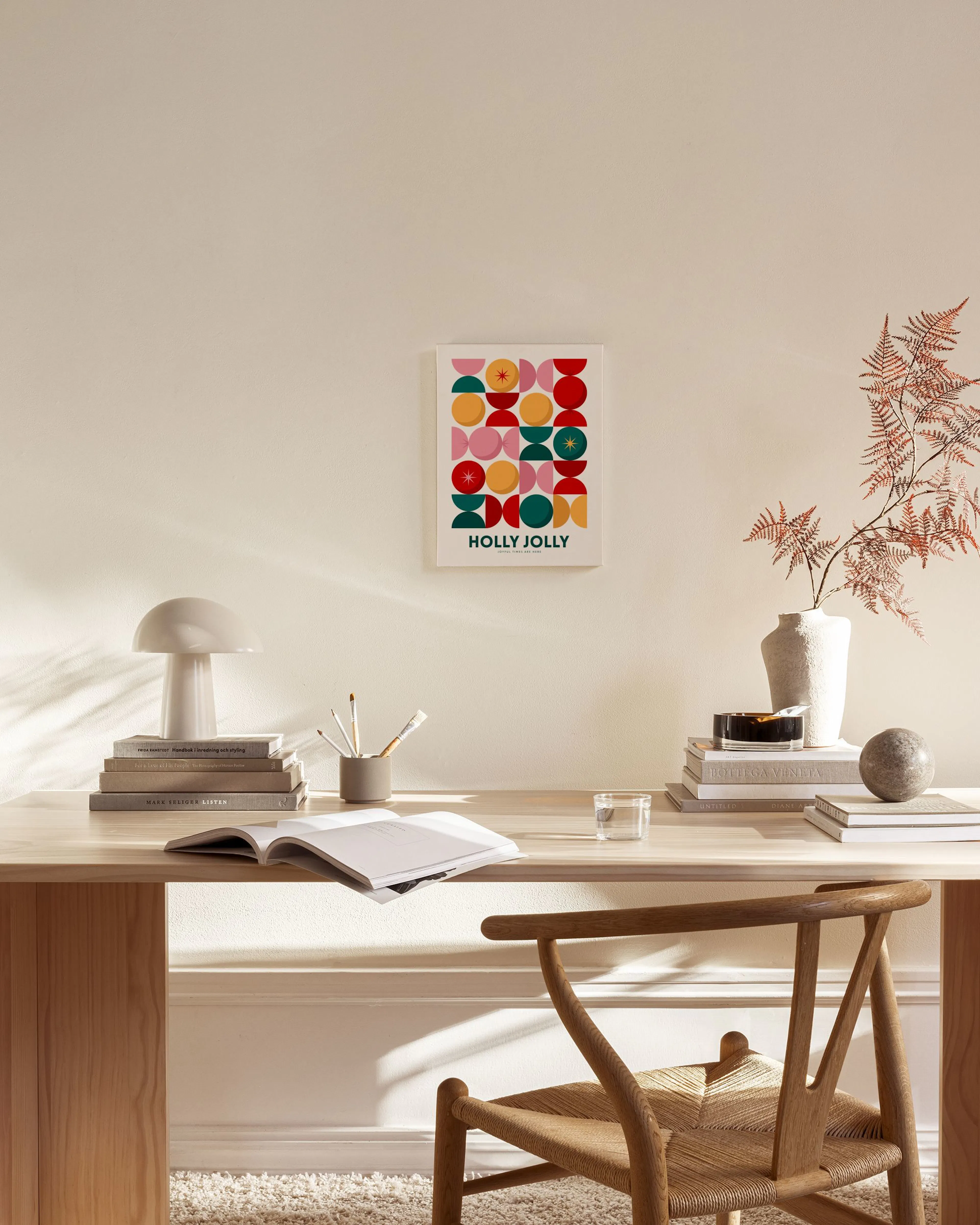 Een canvas met een Holly Jolly-tekst en een patroon van rode, roze, gele en groene halve cirkels en sterren, hangend boven een h