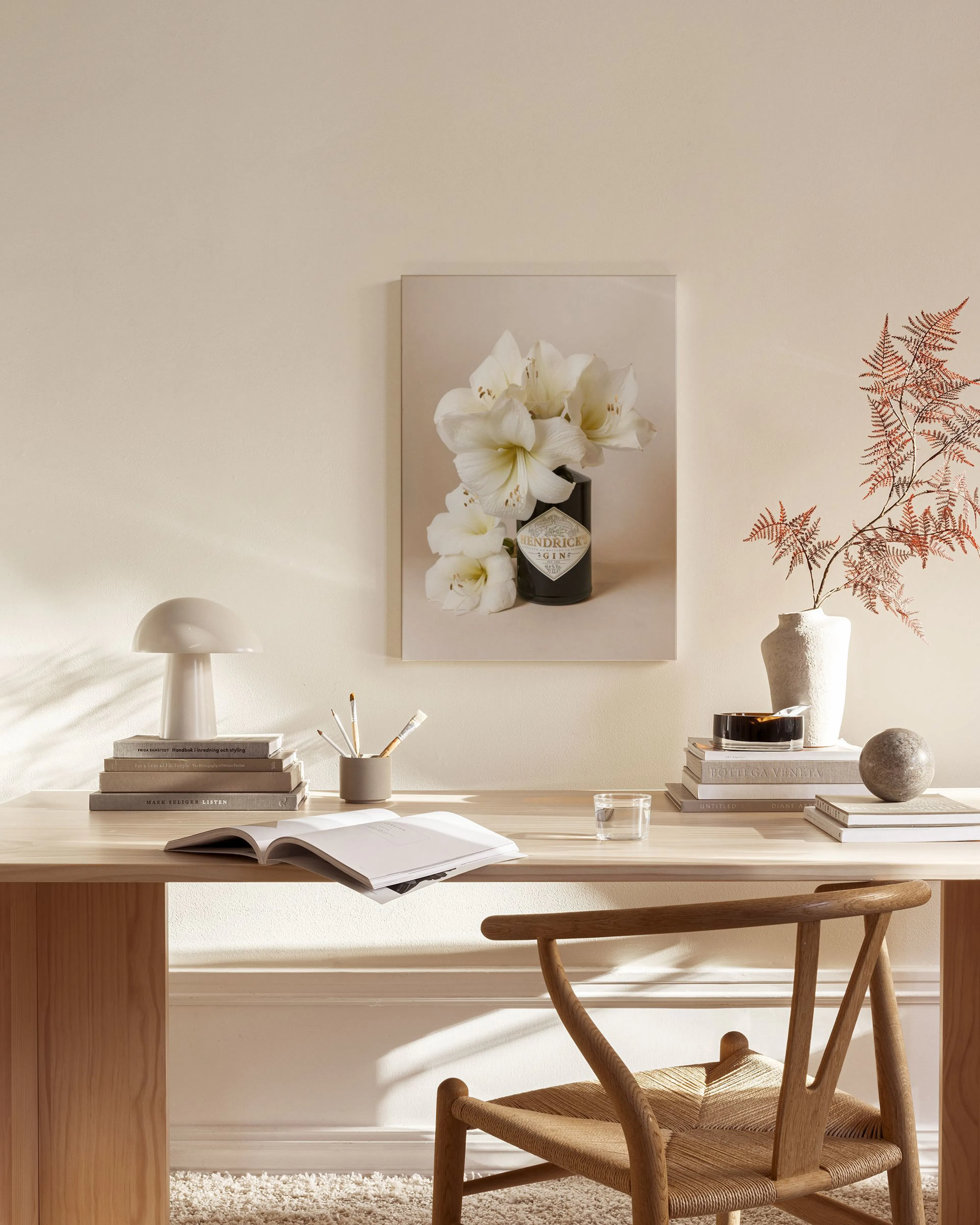 Canvas met witte amaryllissen in een donkere fles, boven een houten dressoir in een lichte woonkamer.