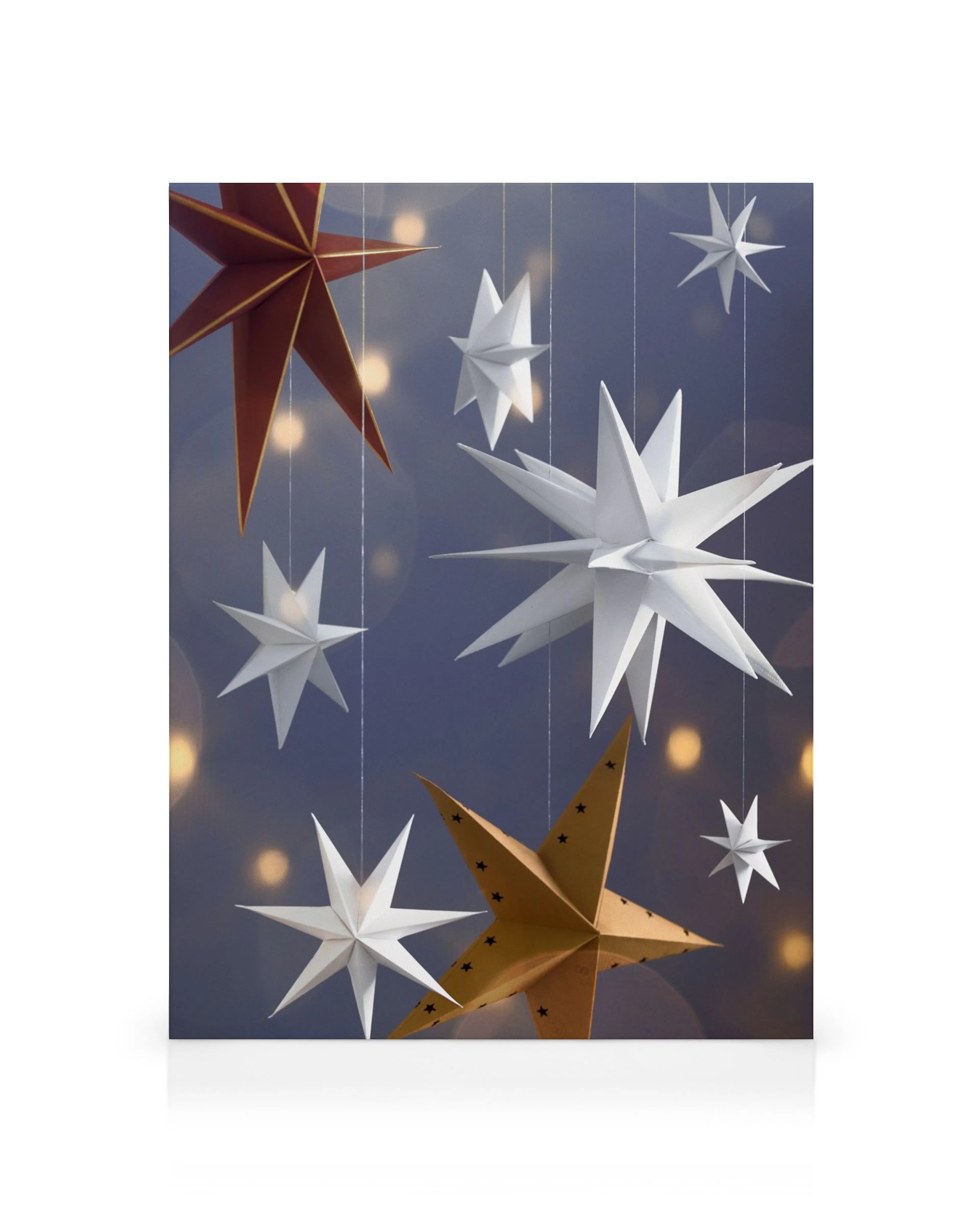 Estrellas de papel colgantes: blancas, rojas y doradas, con fondo azul y luces bokeh, creando un ambiente mágico y festivo.
