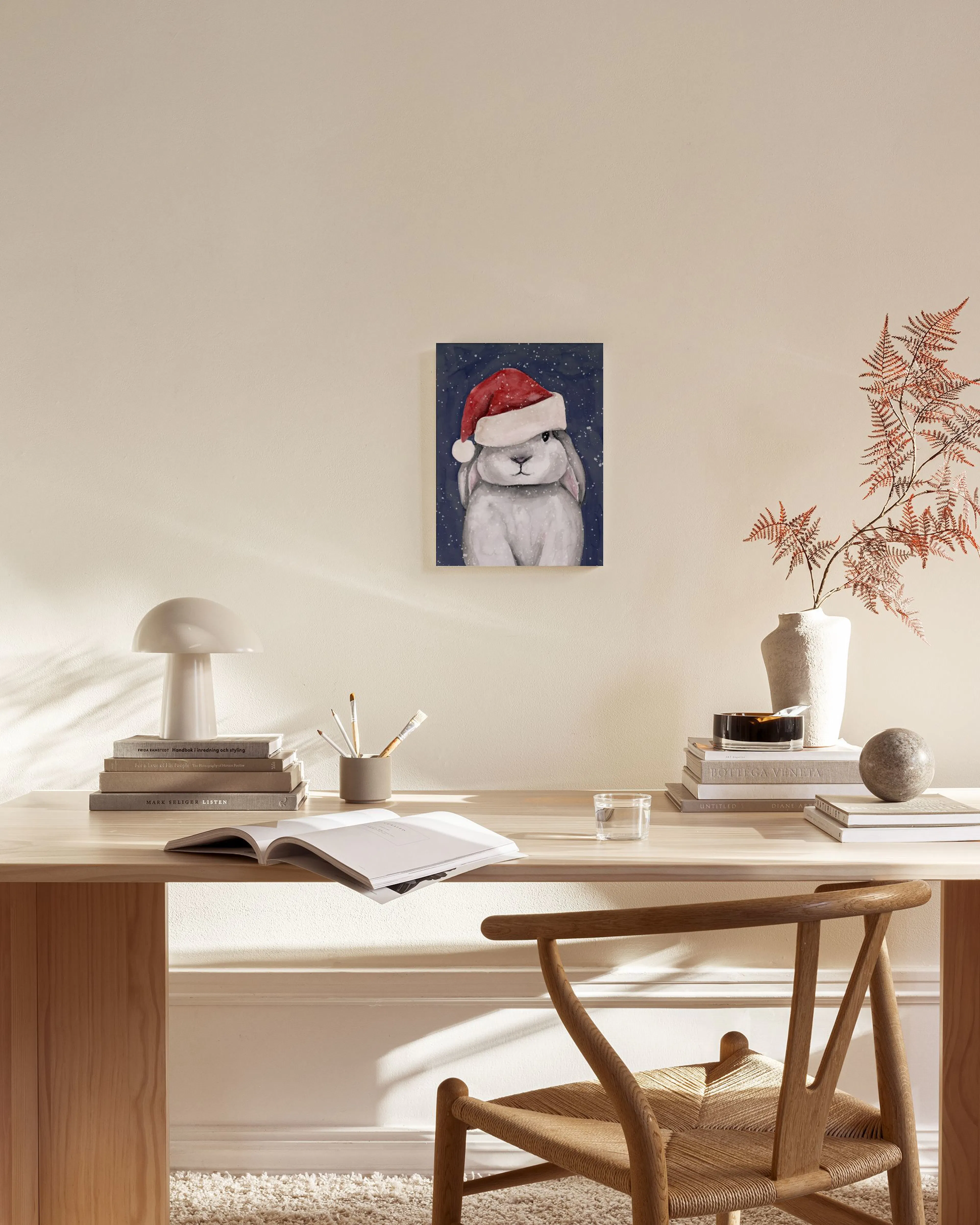 Toile dun lapin gris portant un bonnet de Noël rouge sur fond bleu nuit, accrochée au-dessus dun banc en bois dans un salon.