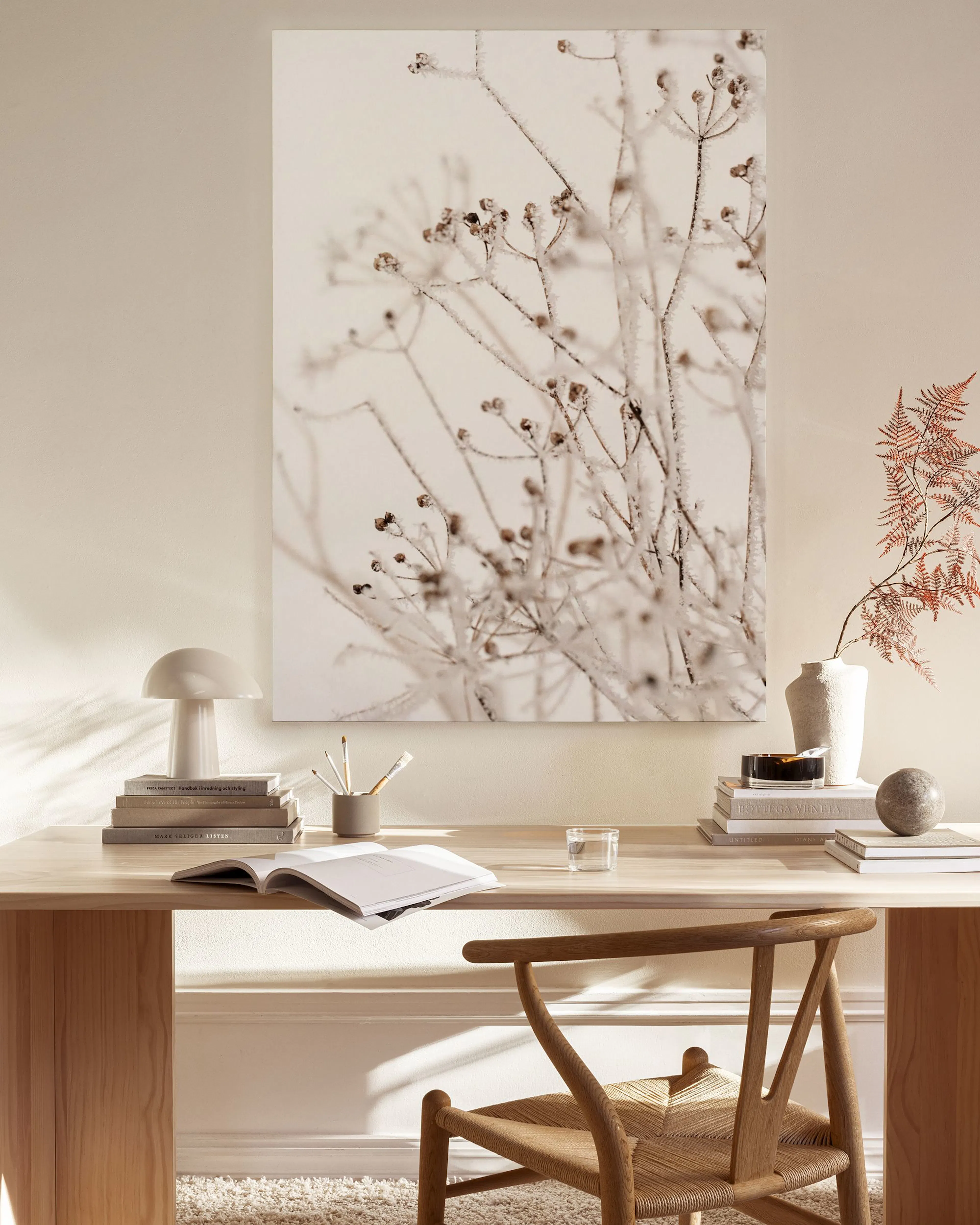 A canvas print of delicate dried plant branches with small seed pods, hanging in a bright, minimalist living room.