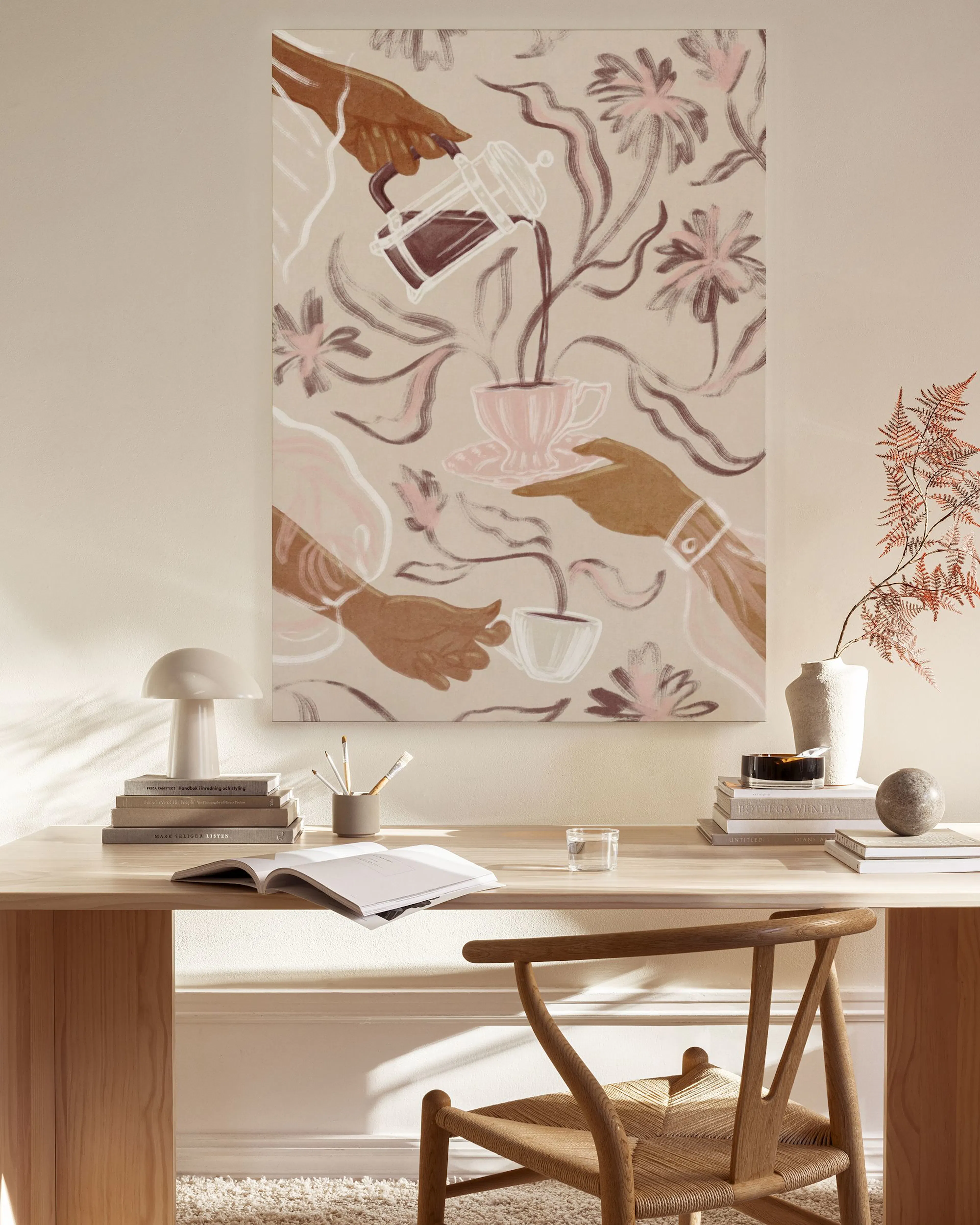 A canvas print of hands pouring coffee into cups among pink and brown flowers, hanging in a bright living room.