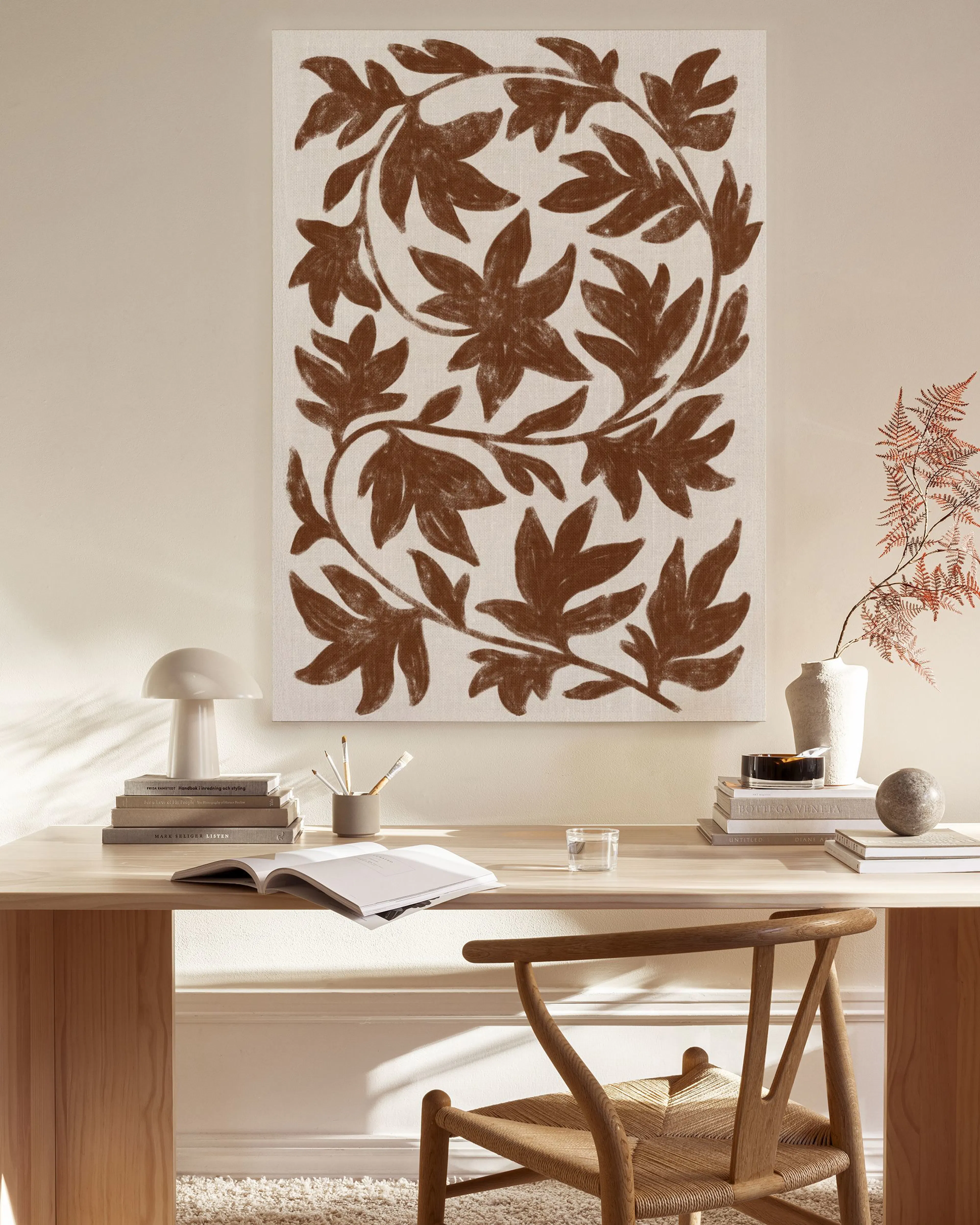 Canvas print of brown stylized leaves forming a circular vine pattern, hanging in a bright, minimalist living room.