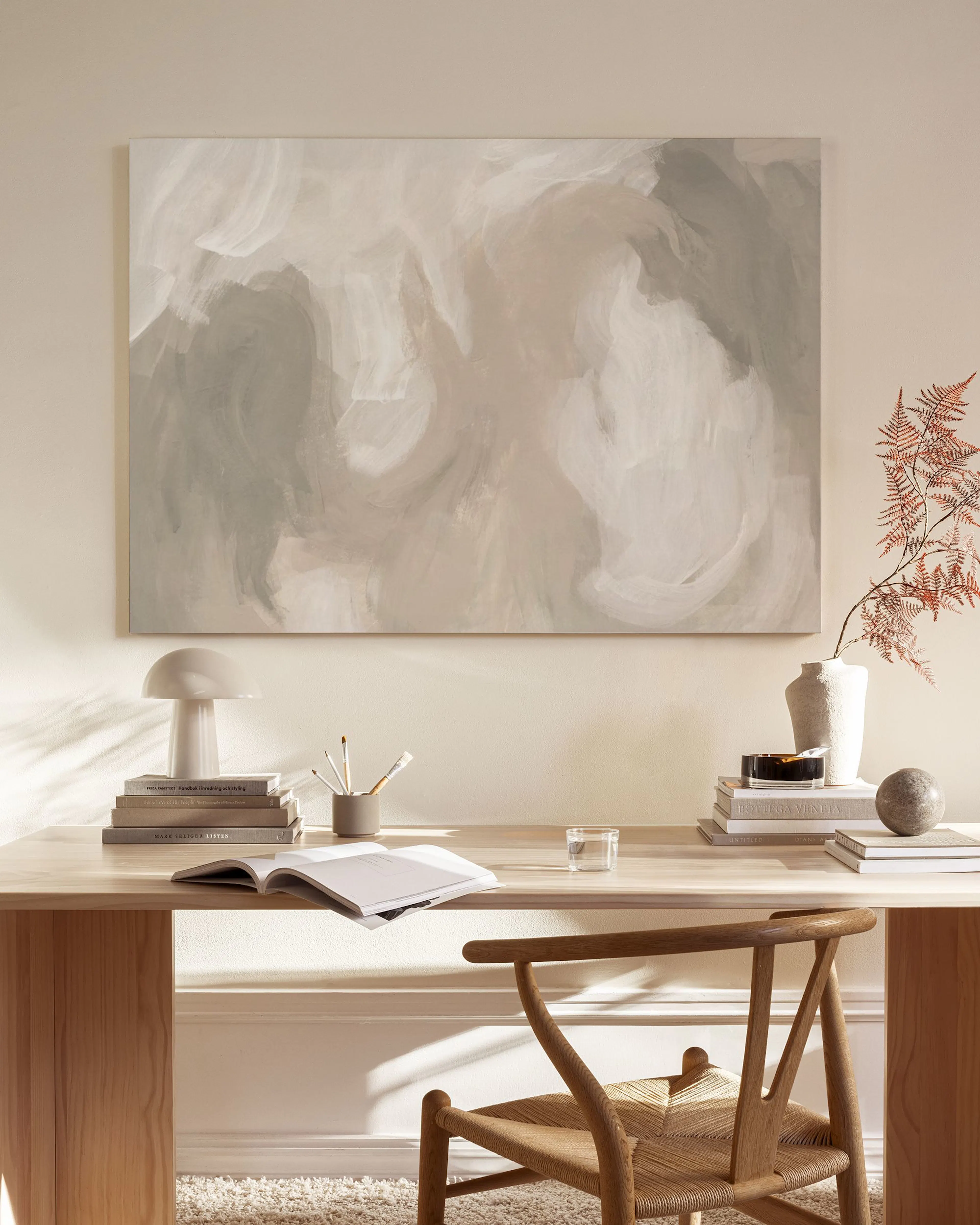 Canvas met abstracte vormen in beige, wit en grijs, hangend boven een houten dressoir in een lichte woonkamer.