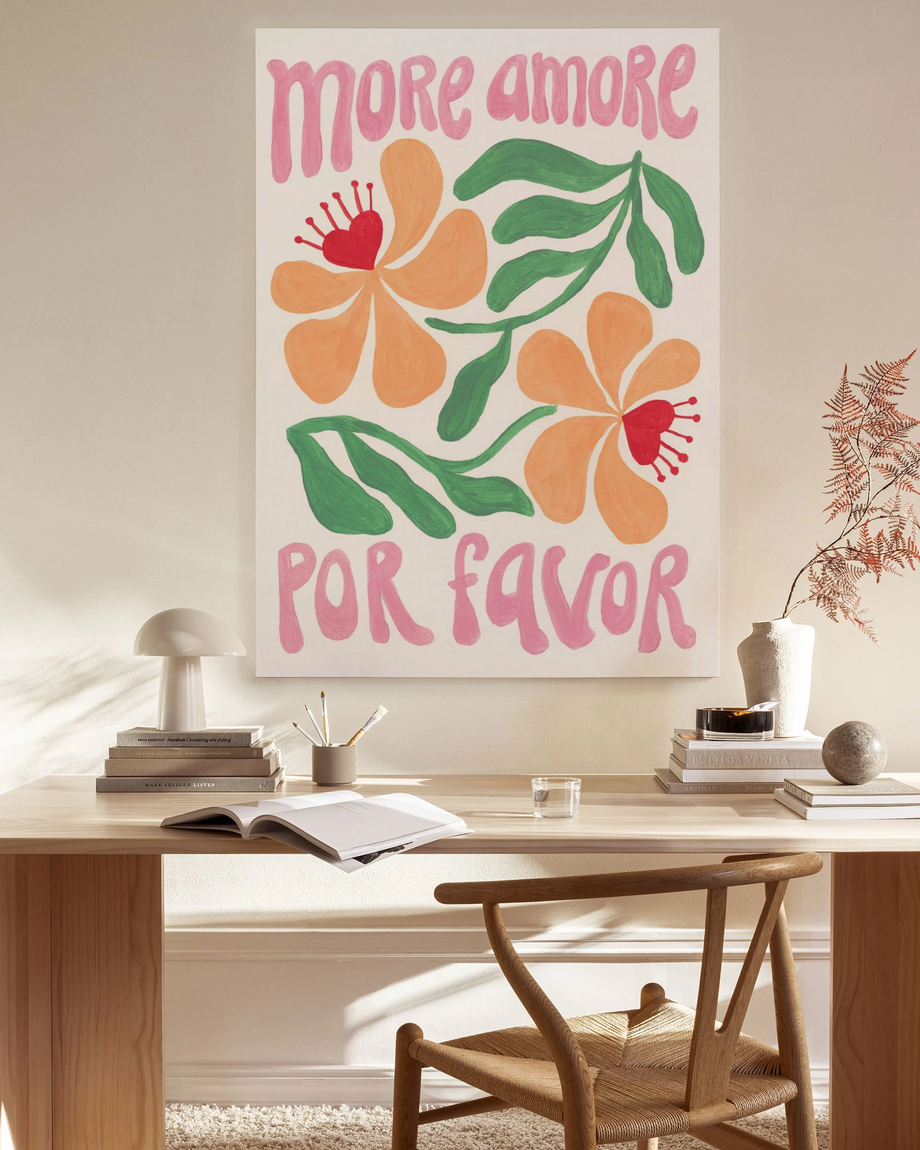 A canvas print with more amore por favor in pink script and orange flowers with green leaves, displayed in a bright living room.