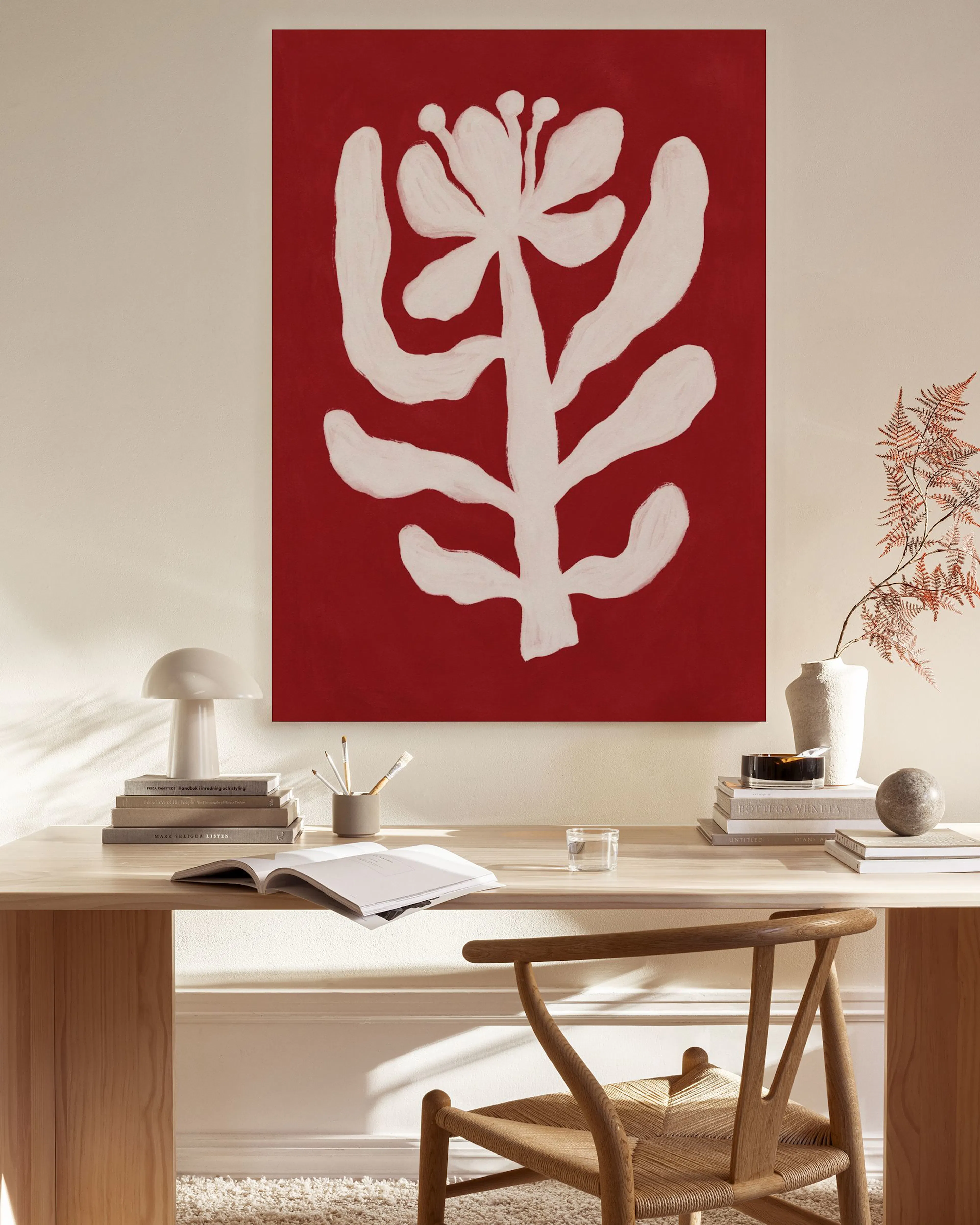 Toile rouge avec motif végétal blanc stylisé, accrochée au mur dun salon moderne avec fauteuil en bois et table basse.