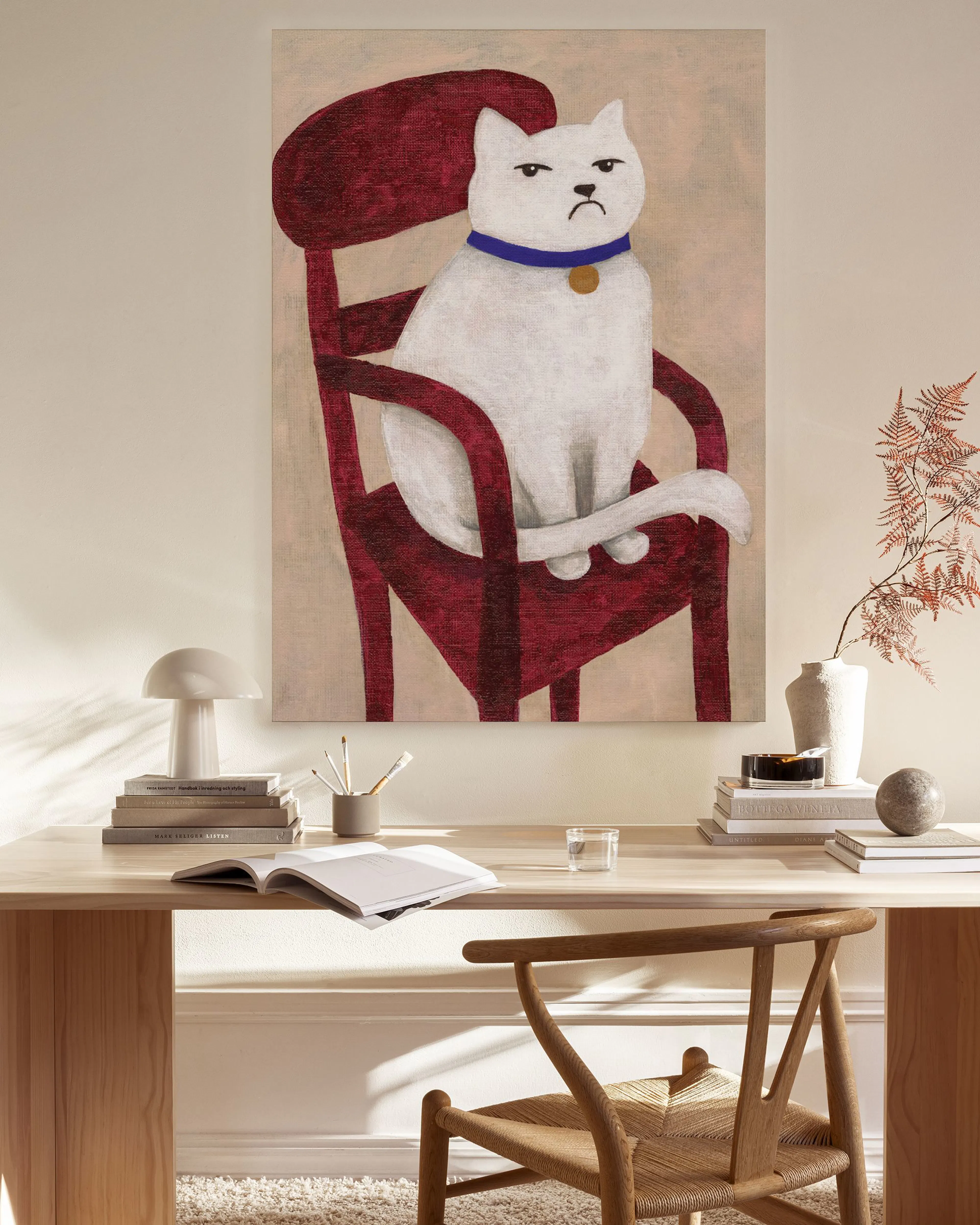A canvas print of a grumpy white cat with a blue collar, sitting on a red chair, hanging in a minimalist living room.