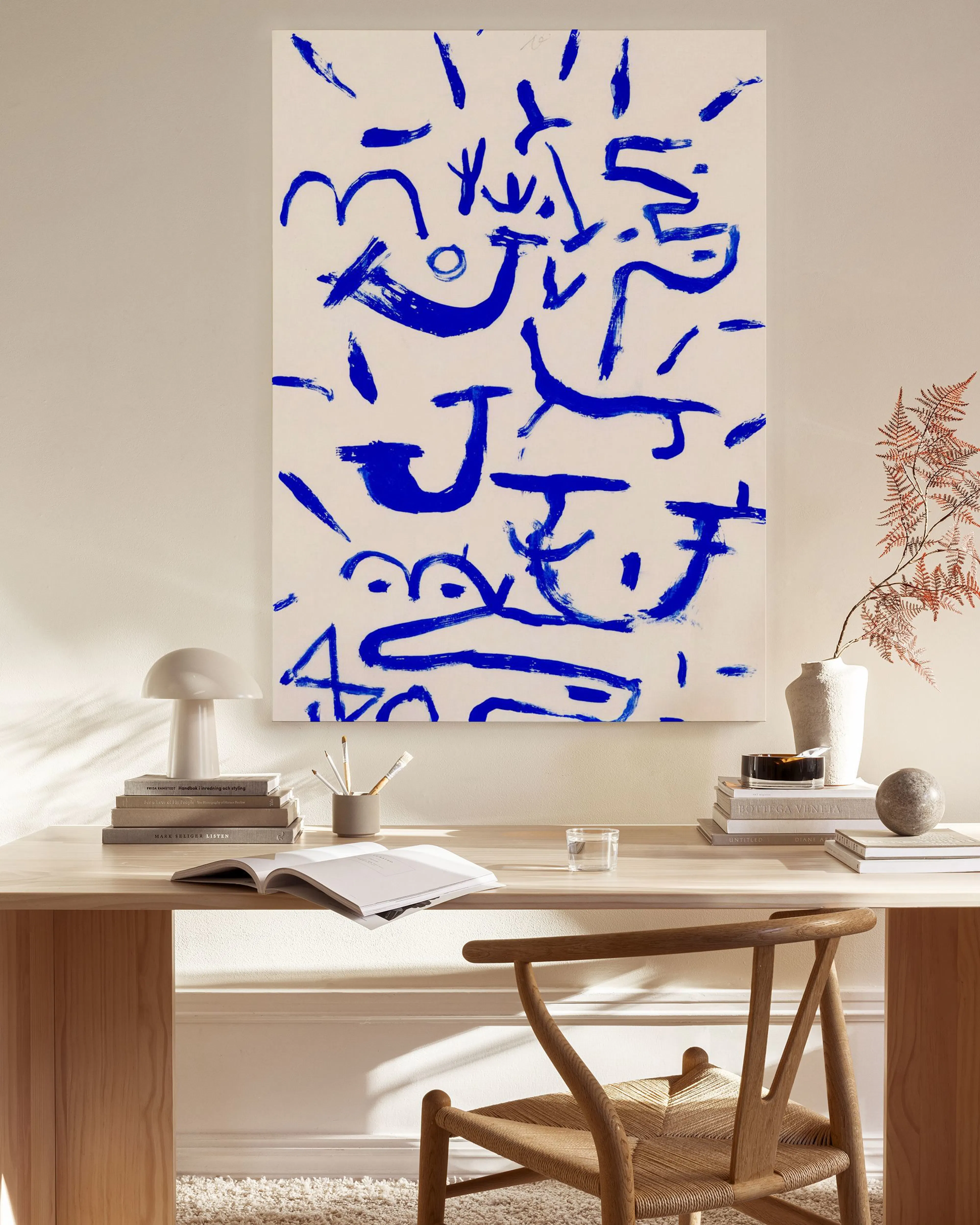 Stampa su tela astratta con forme e linee blu, appesa in un moderno soggiorno sopra una panca in legno.