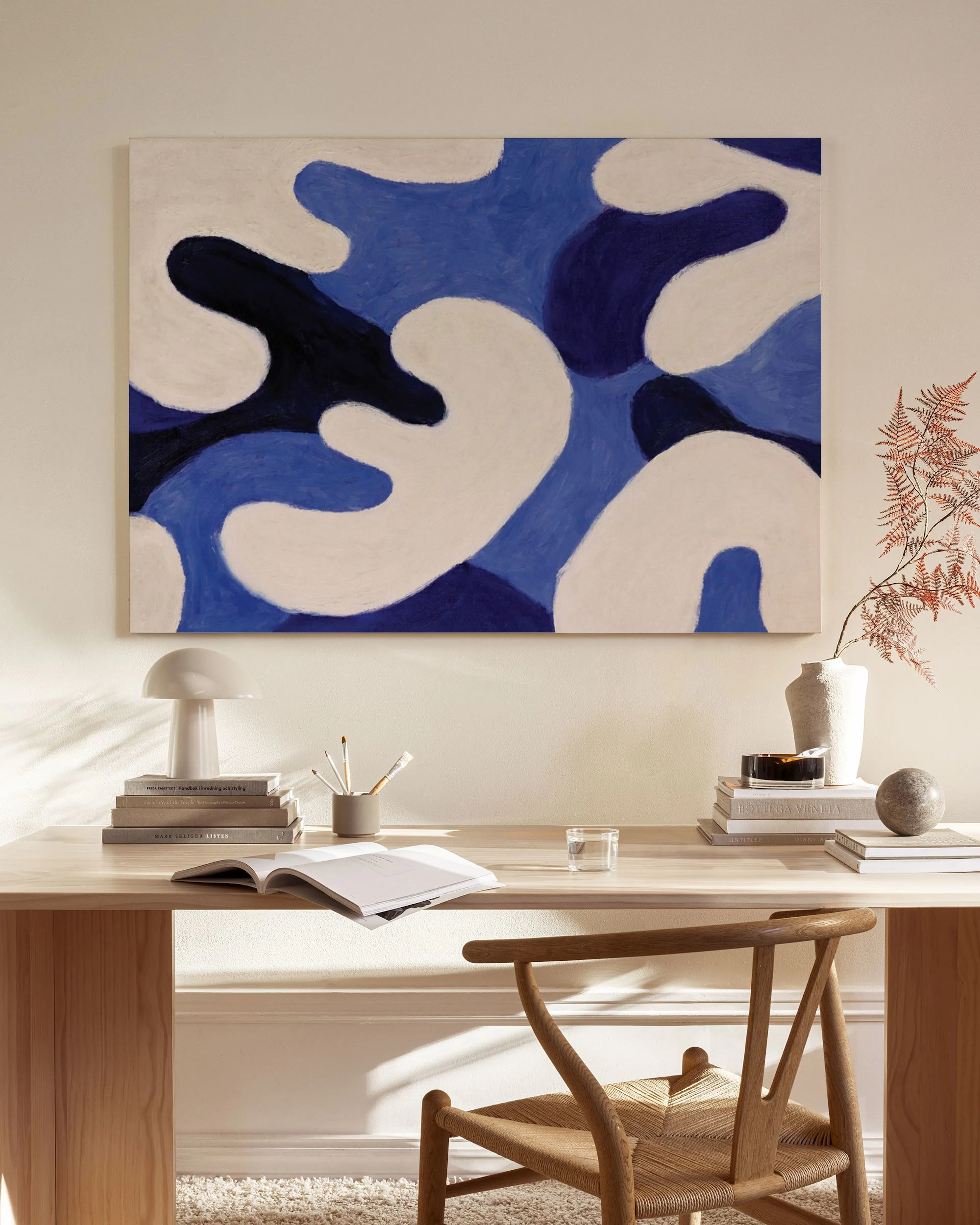 Canvas met organische vormen in blauw, donkerblauw en wit, hangend boven een houten dressoir in een lichte woonkamer.