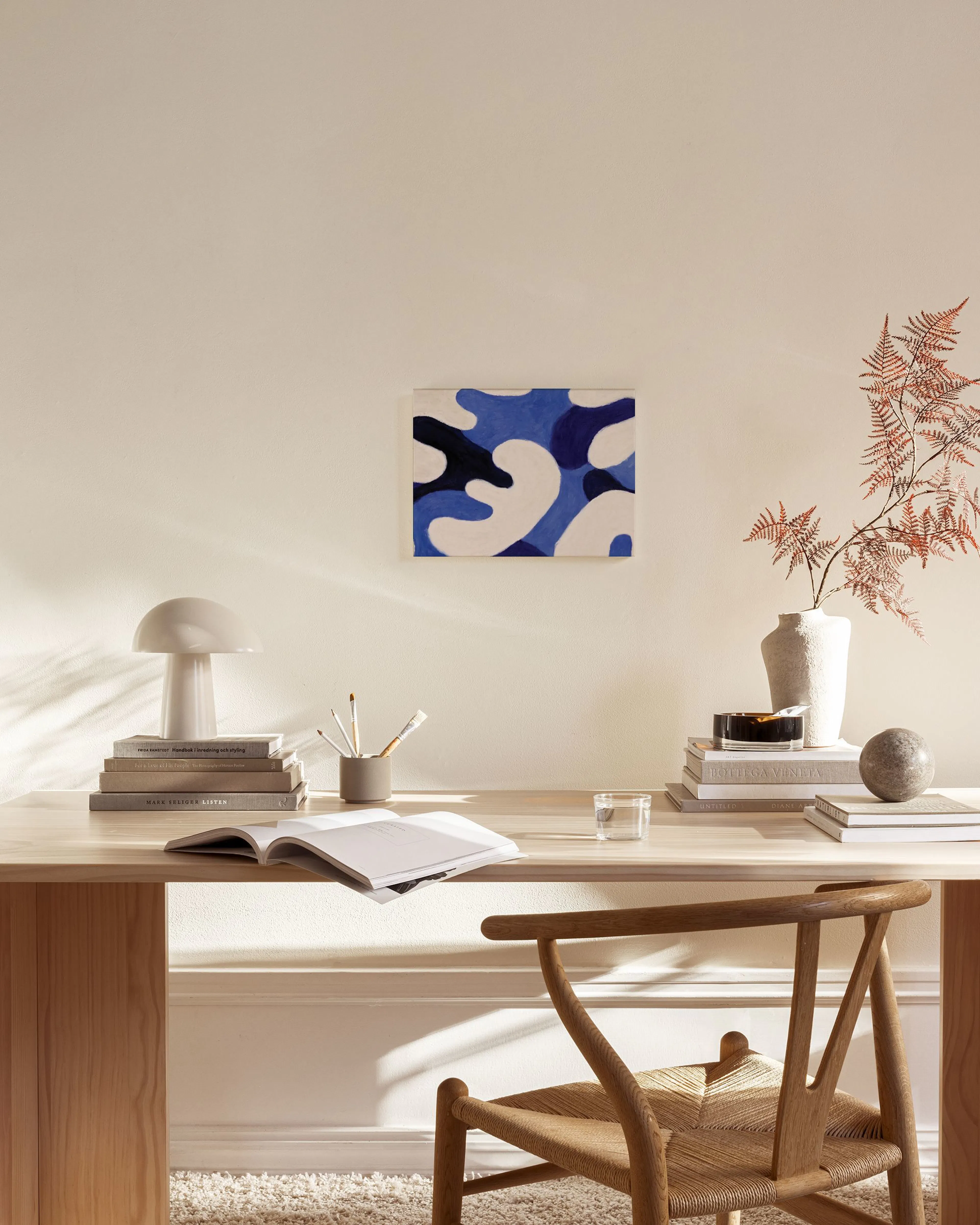 Tela decorativa com formas orgânicas azuis, brancas e pretas, exibida numa sala de estar minimalista acima de um móvel de madeir