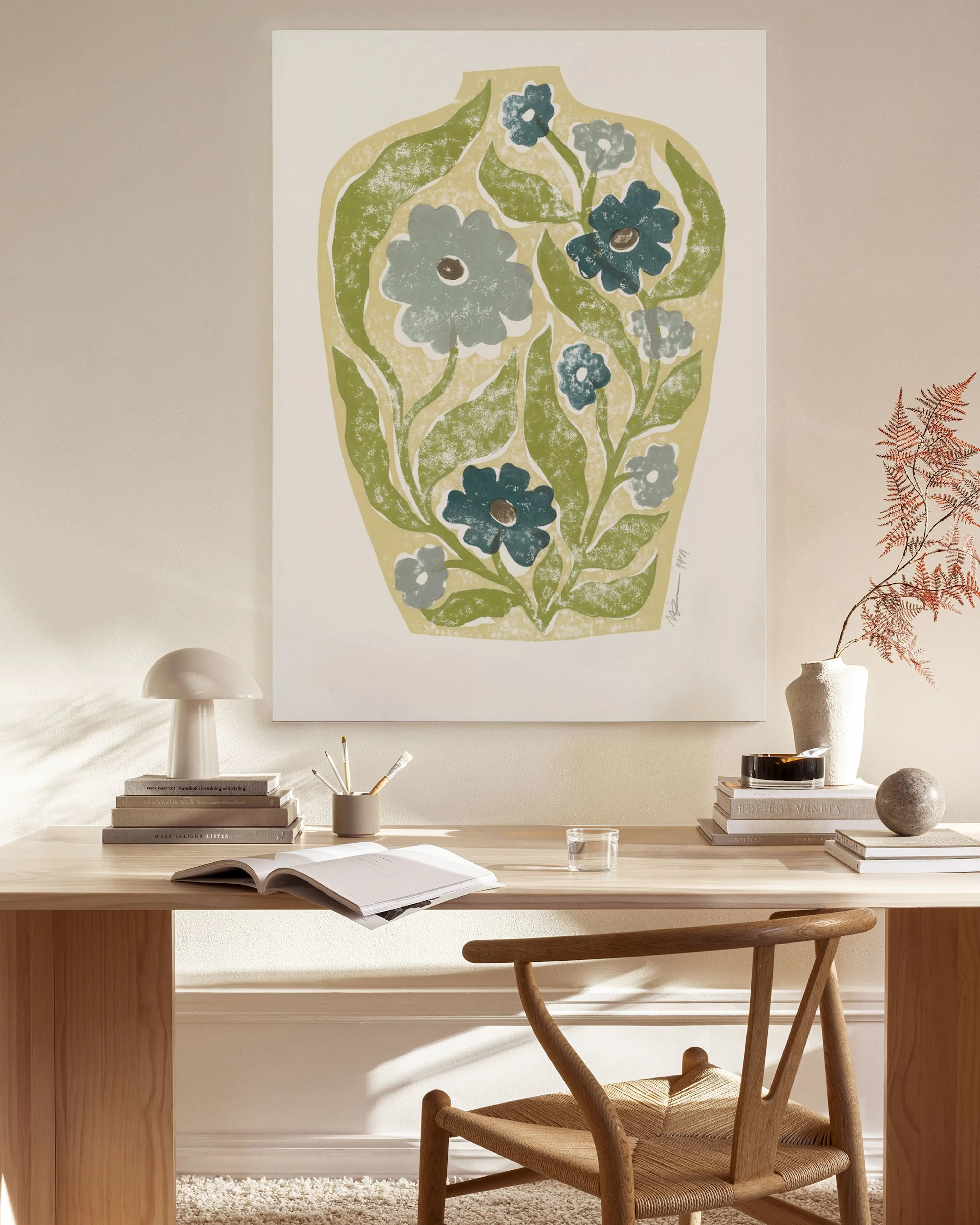 Botanical vase print with blue and gray flowers, and green leaves, hanging in a neutral modern living room.