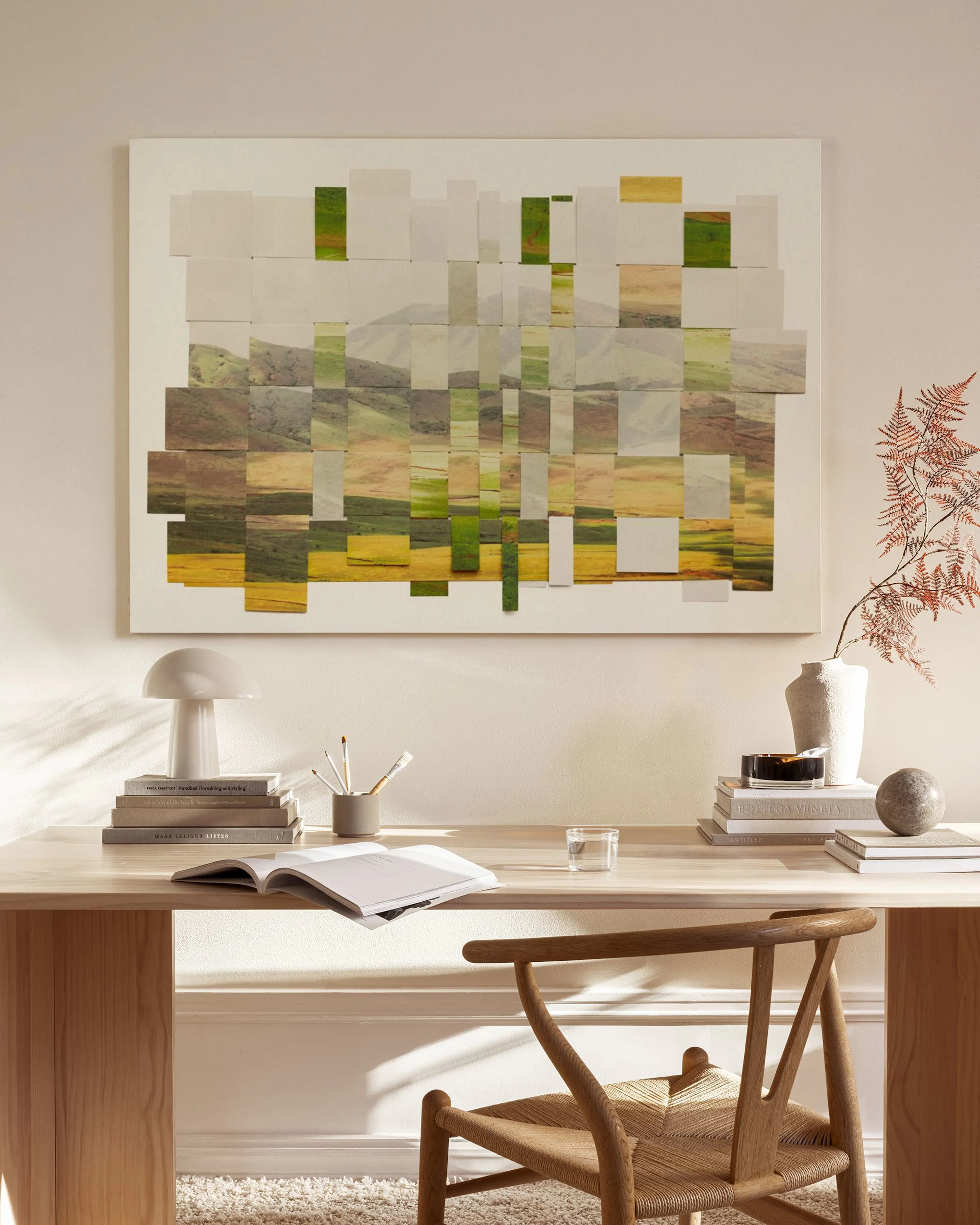 Abstract landscape print with green and yellow pixelated fields, hanging in a minimalist living room above a wooden console.