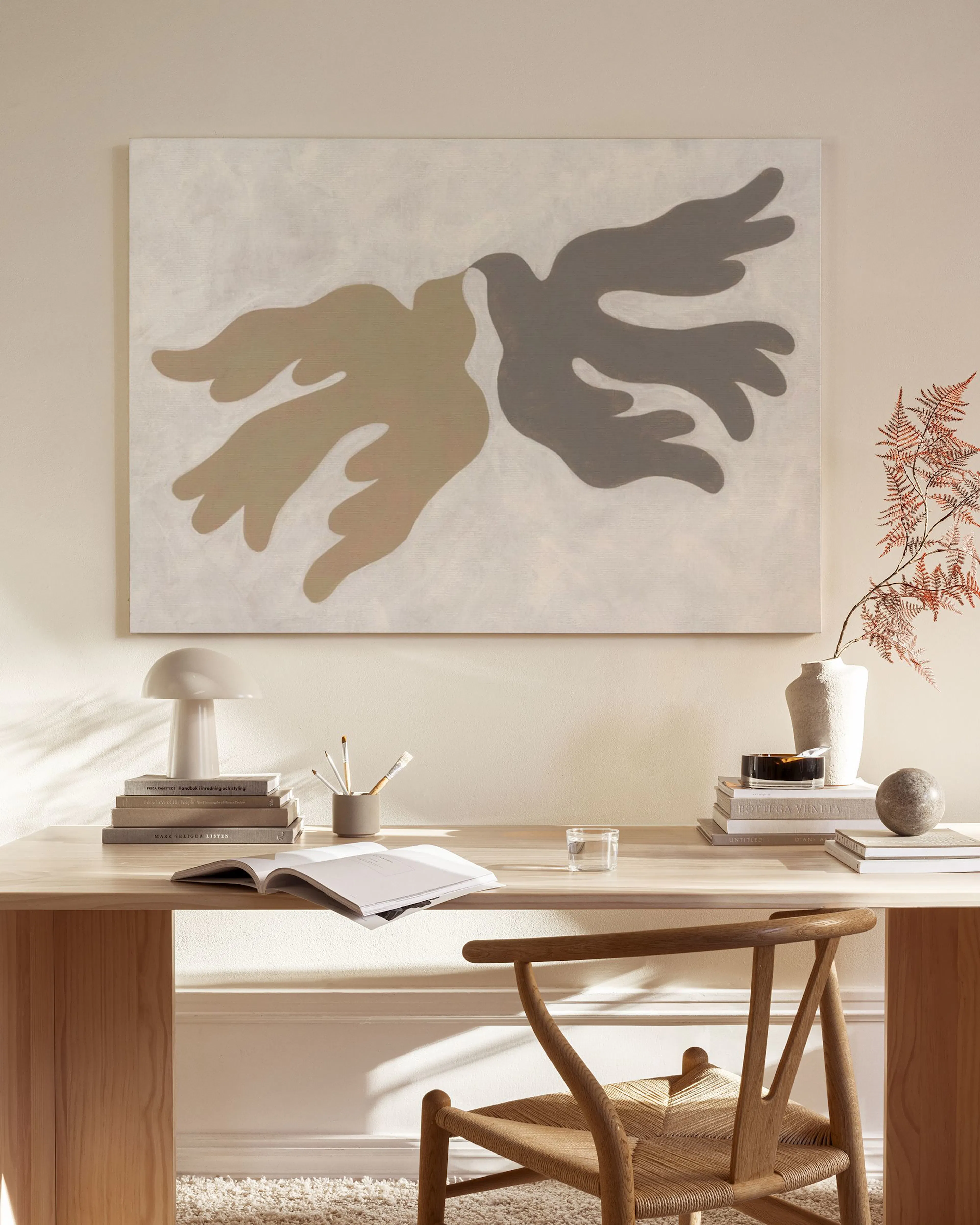 Lienzo abstracto con formas orgánicas beige y gris oscuro sobre un fondo claro, colgado en una sala de estar minimalista.