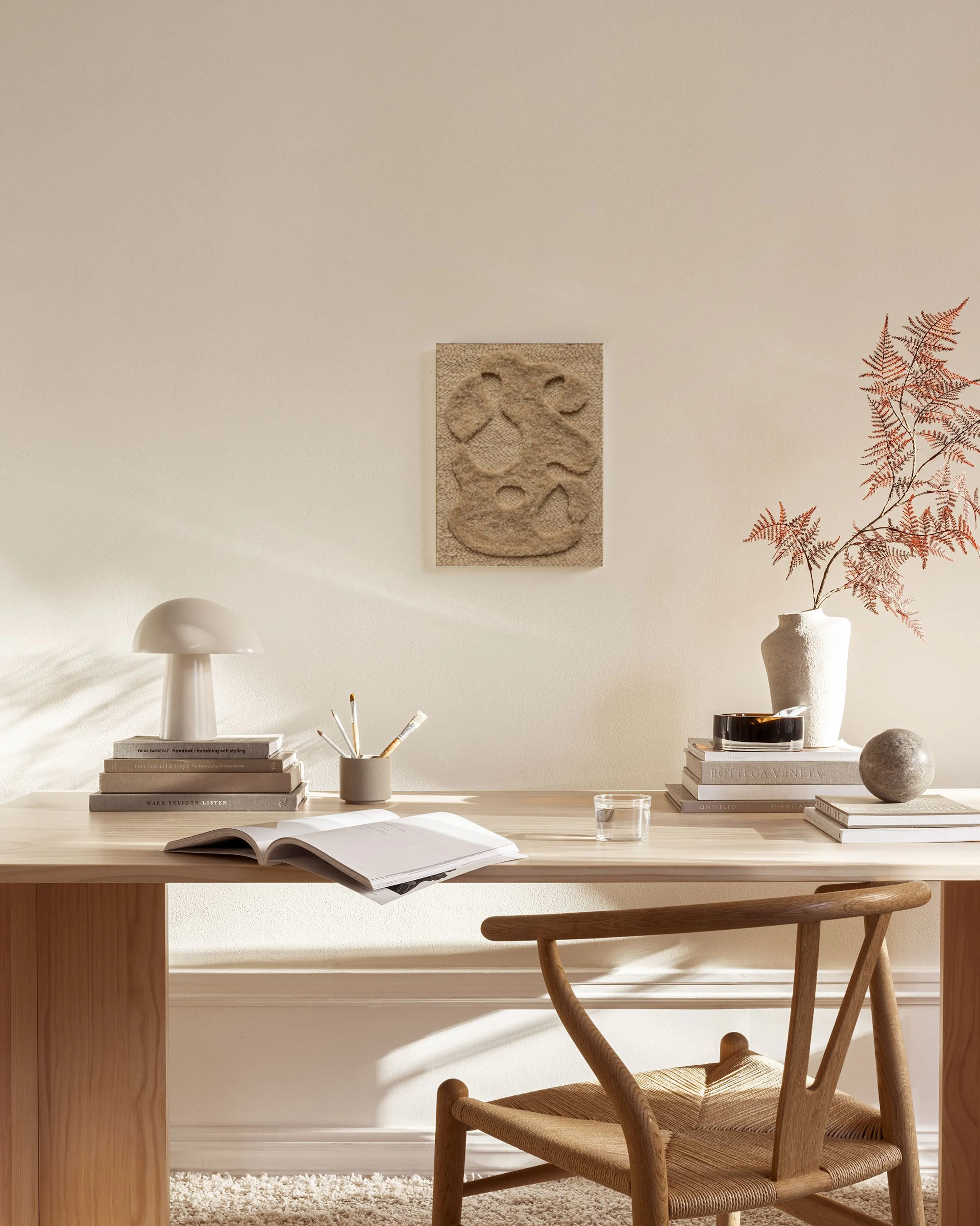 Lienzo texturizado beige con formas orgánicas abstractas colgado sobre un mueble bajo en una sala de estar minimalista.