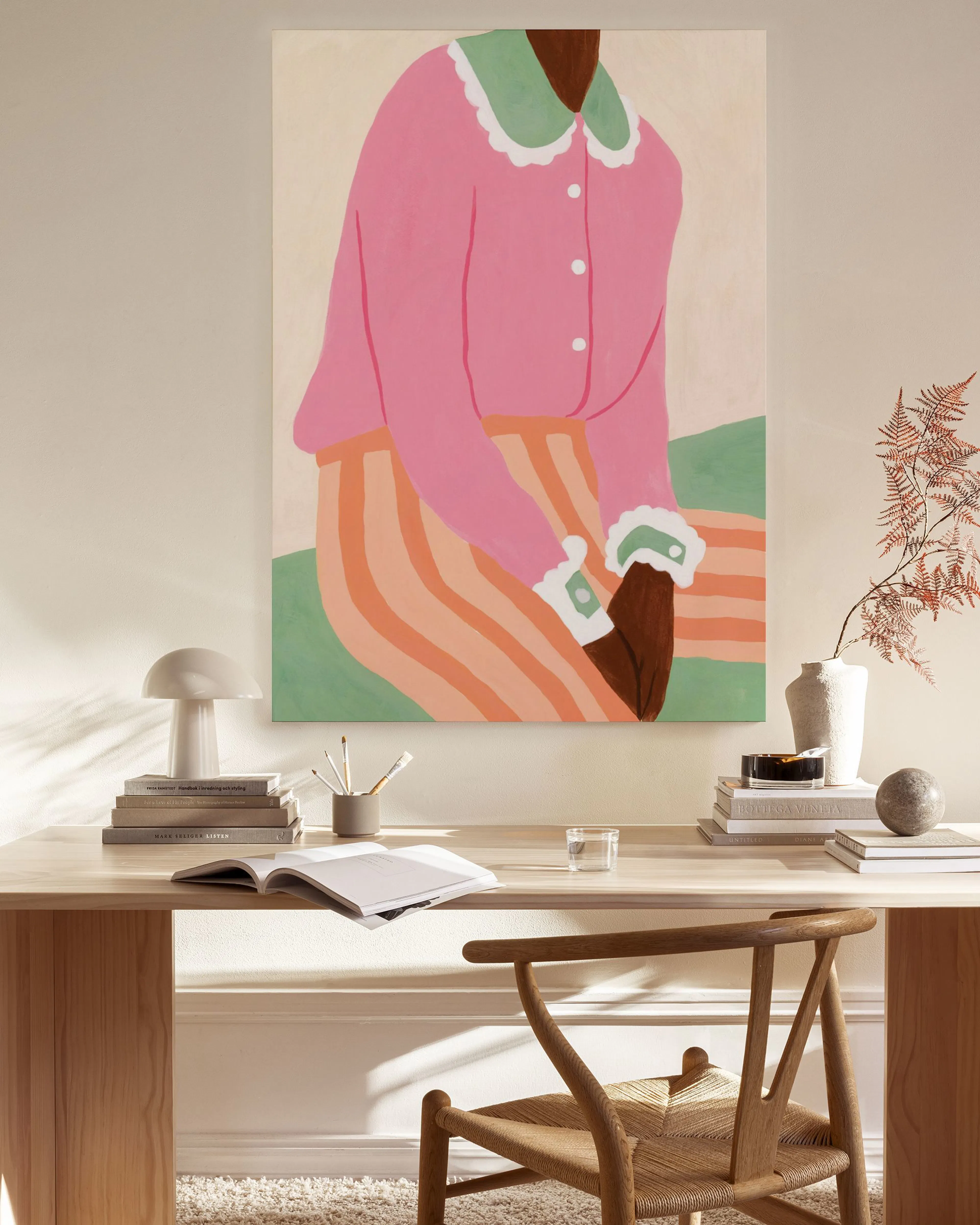 Toile dune silhouette assise en chemise rose et pantalon rayé, accrochée dans un salon moderne et lumineux.