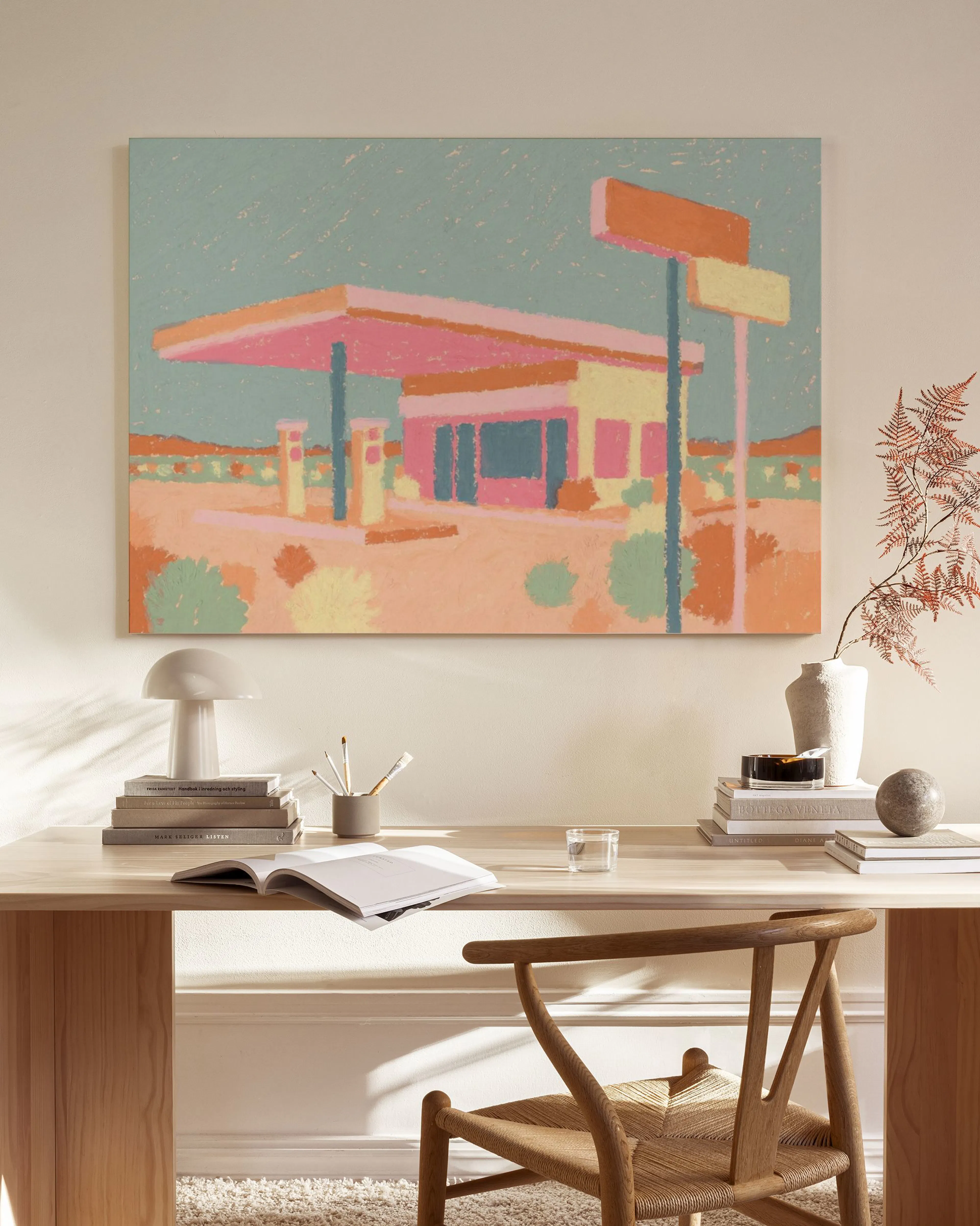 Toile dune station-service désertique aux teintes pastel roses, bleues et oranges, accrochée au-dessus dun meuble en bois clair 