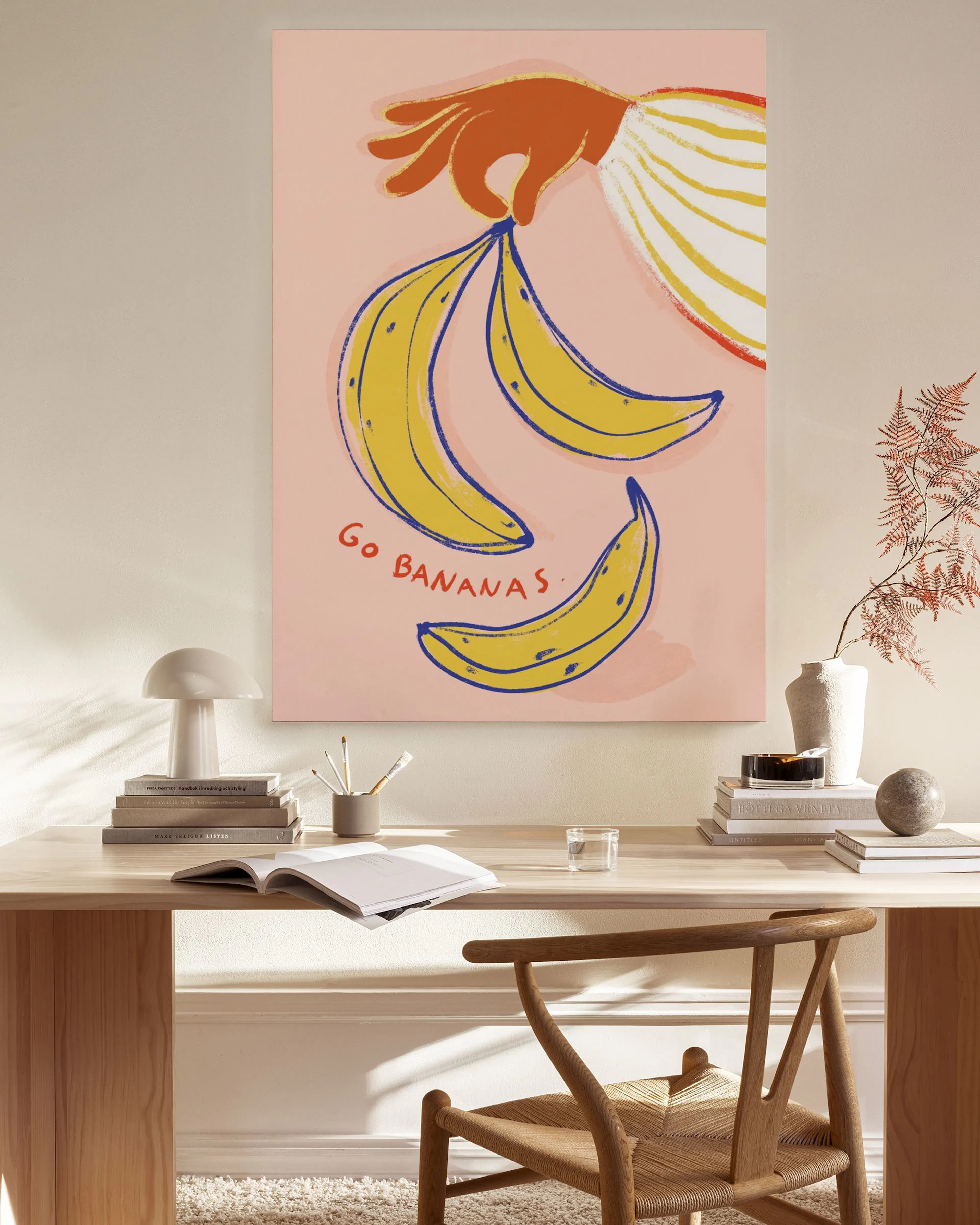 Leinwandbild mit Hand, Bananen und Schriftzug Go Bananas“ im Wohnzimmer über einem Sideboard.