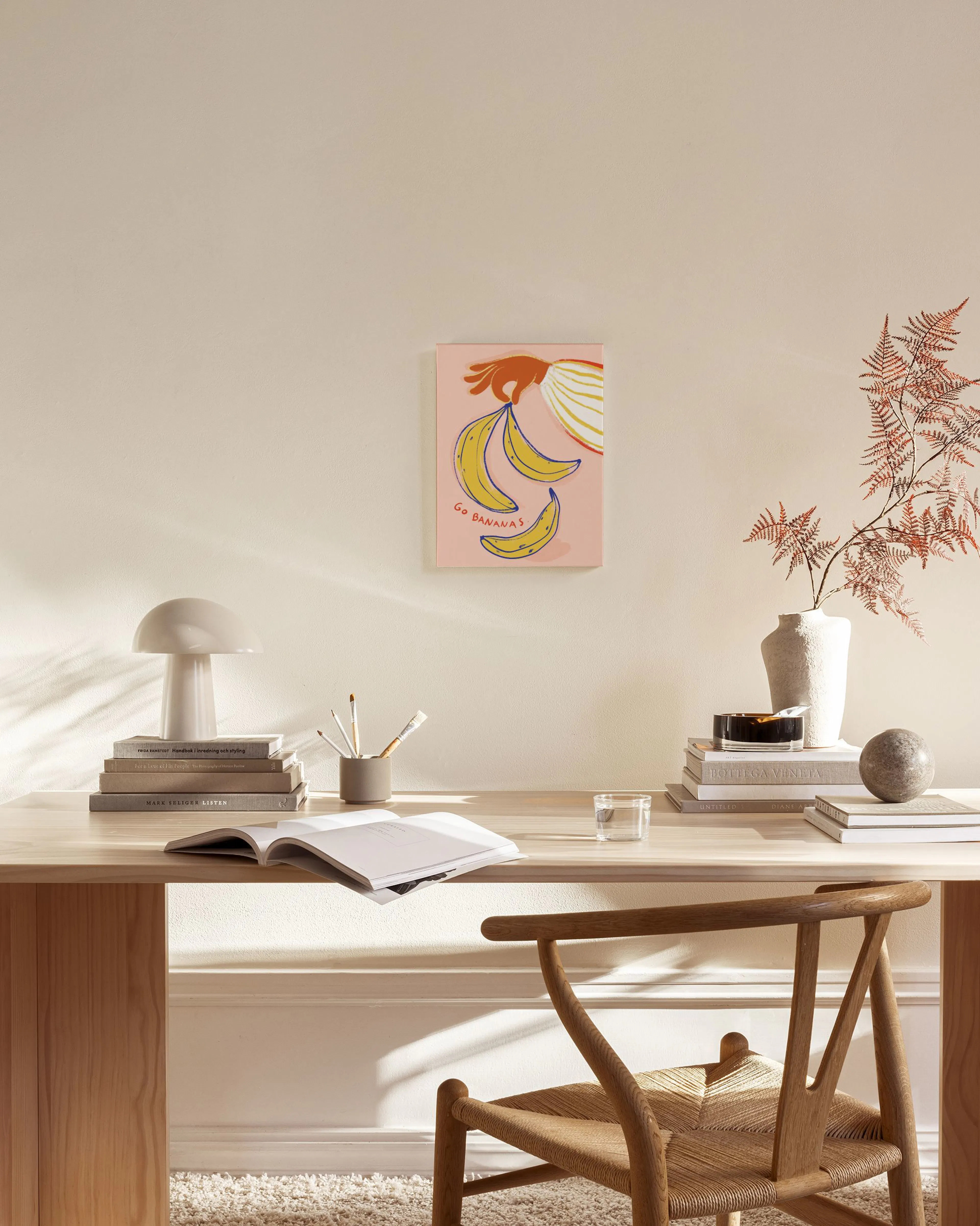 Stampa su tela con mano che tiene banane su sfondo rosa, con scritta Go Bananas, appesa in un salotto moderno.