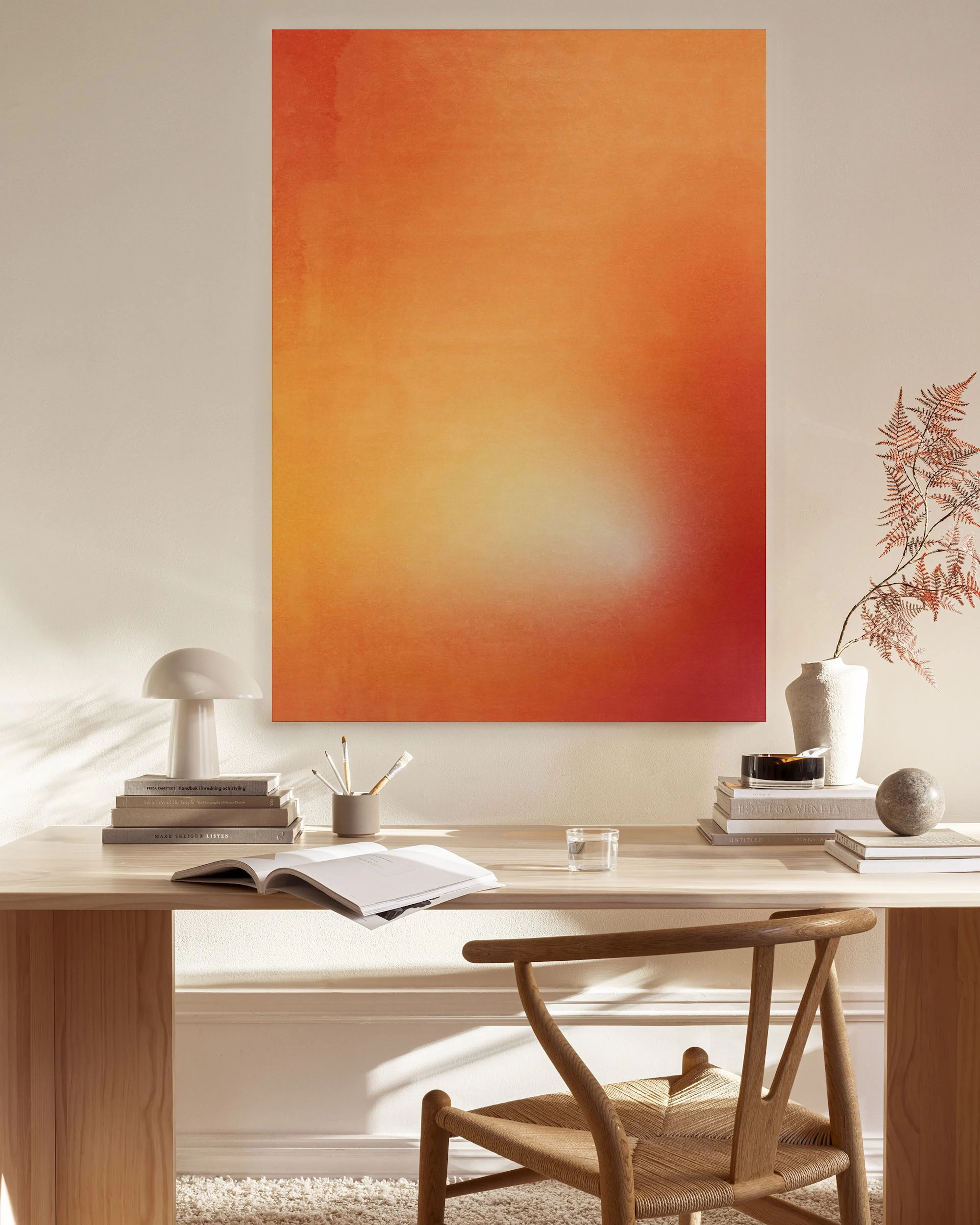 An orange, yellow, and red gradient canvas print, illuminated from the bottom, hanging in a minimalist living room above a woode