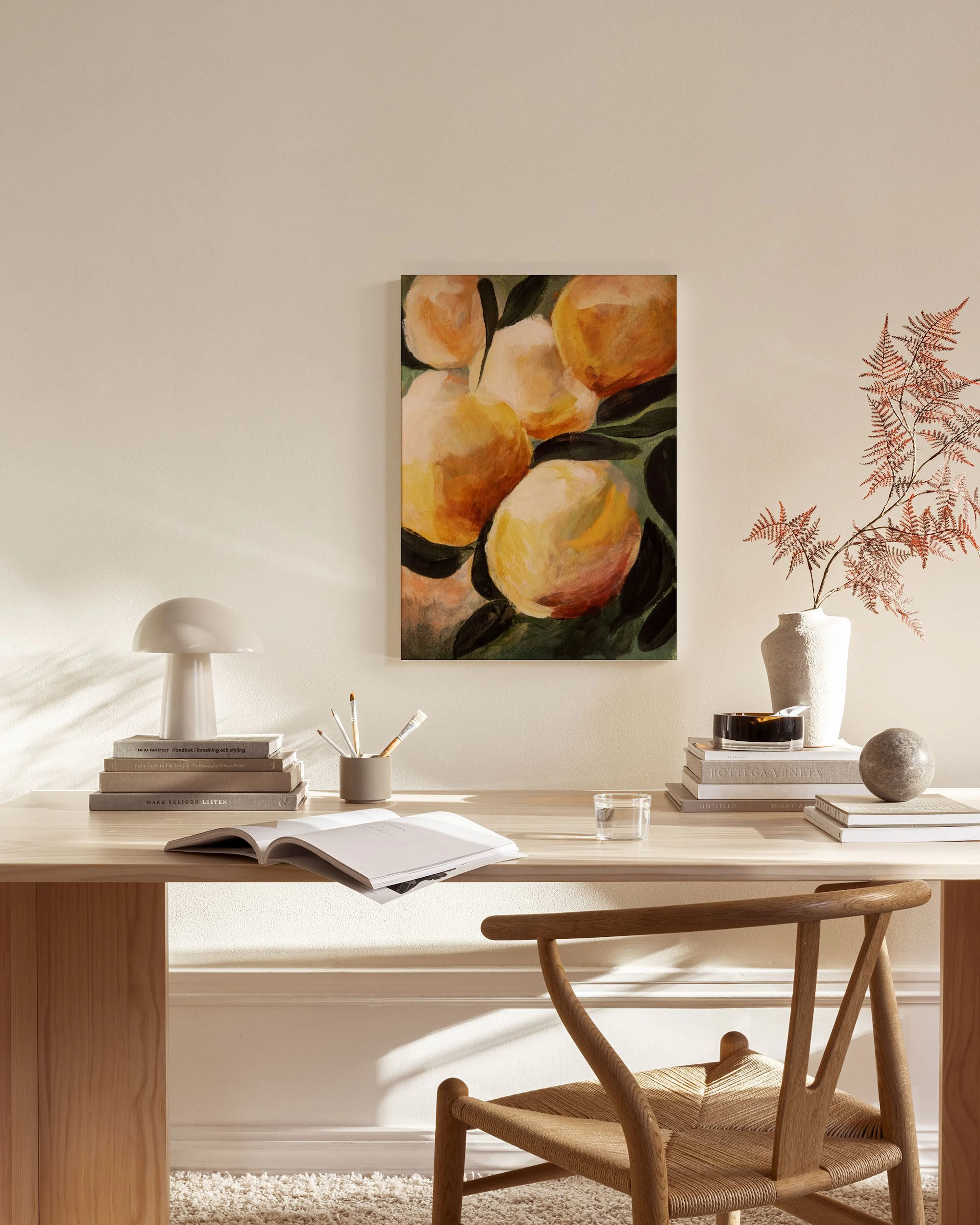 Abstract canvas print of yellow and orange lemons with green leaves, hanging in a bright, minimalist living room.
