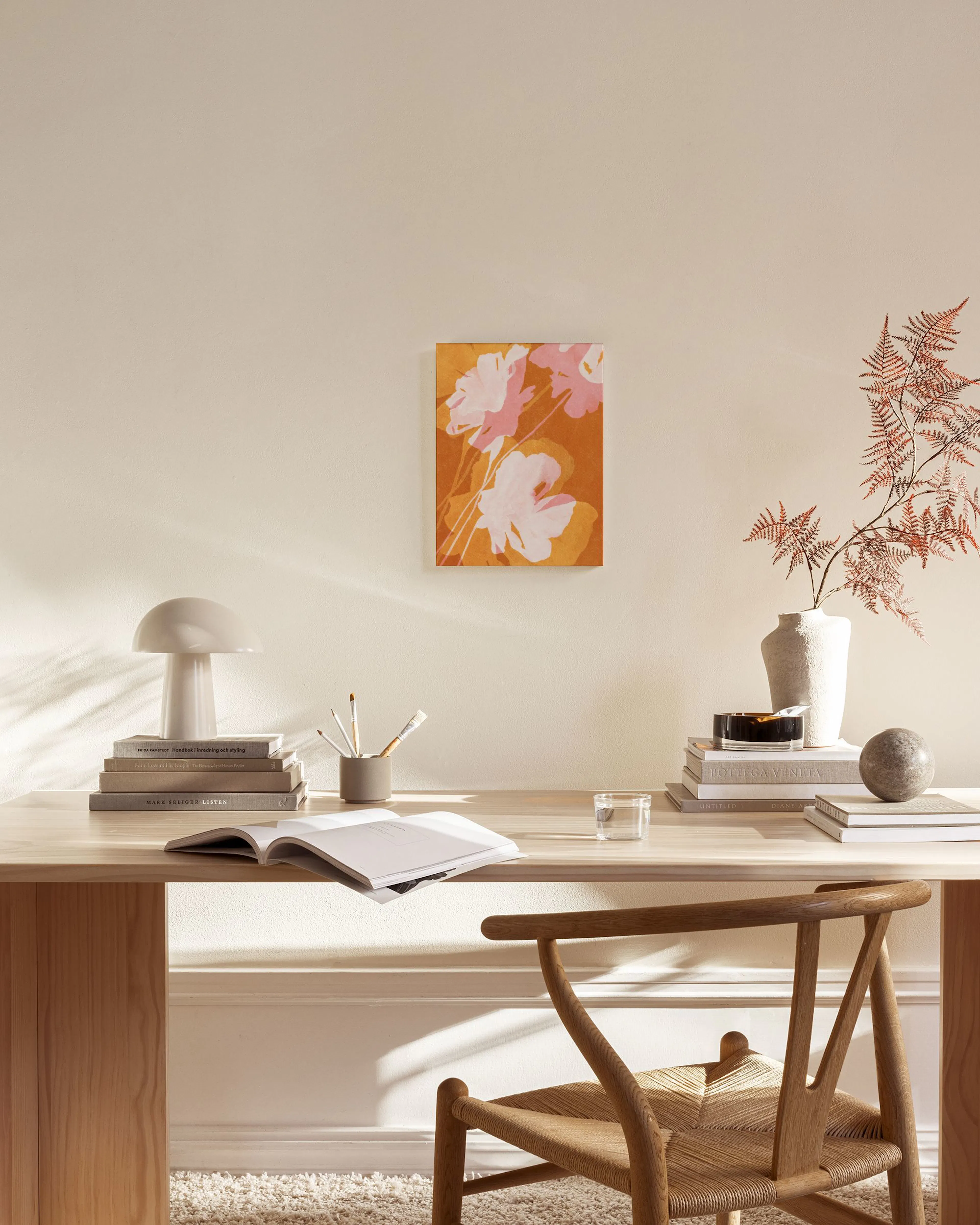 Lienzo con flores rosas y blancas sobre fondo naranja y amarillo colgado en una sala de estar minimalista.