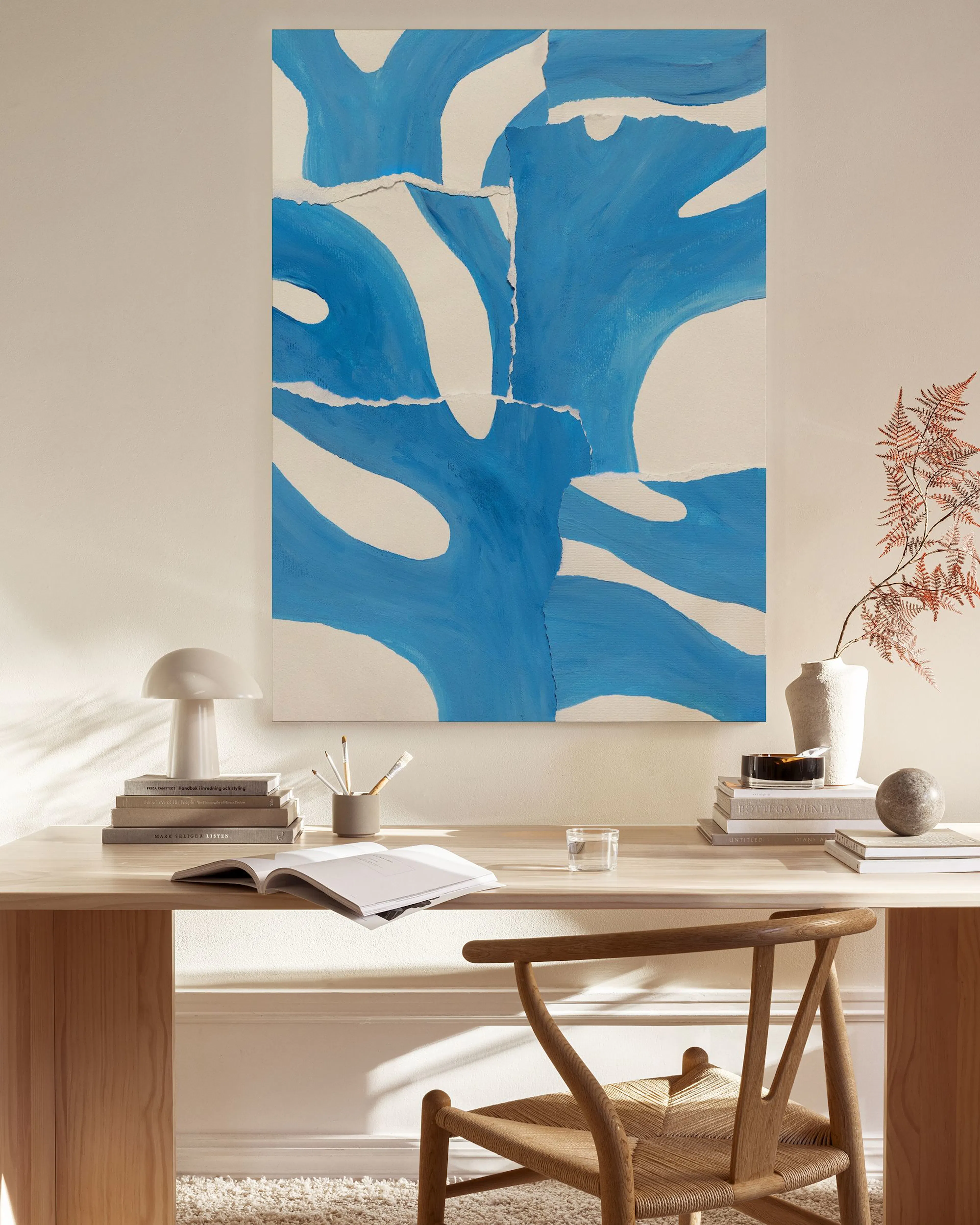 Toile abstraite bleue et blanche suspendue dans un salon moderne avec fauteuil en bois, table basse et lampe.