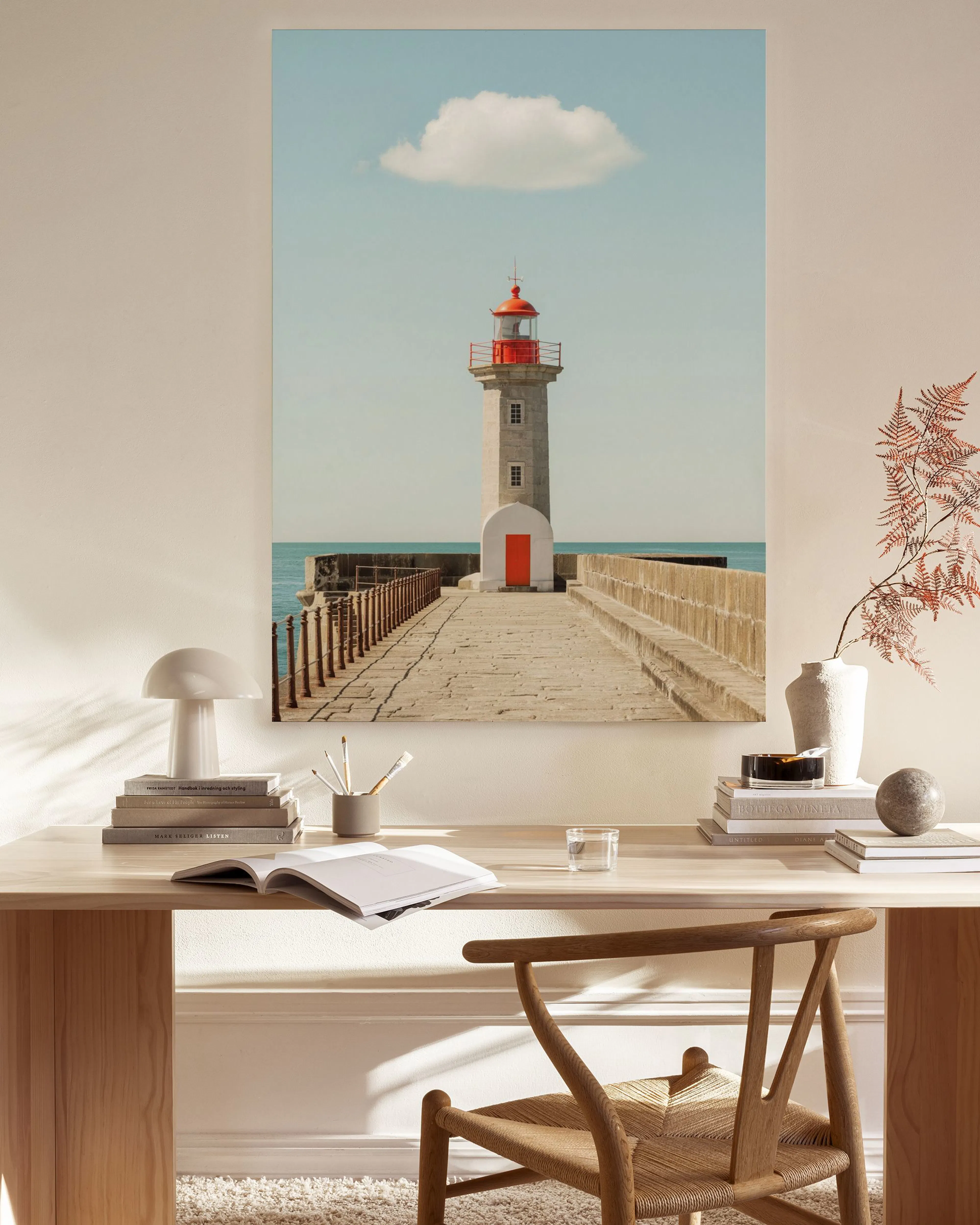 Toile dun phare rouge et blanc sur une jetée, sous un ciel bleu avec un nuage, exposée dans un salon moderne et lumineux.