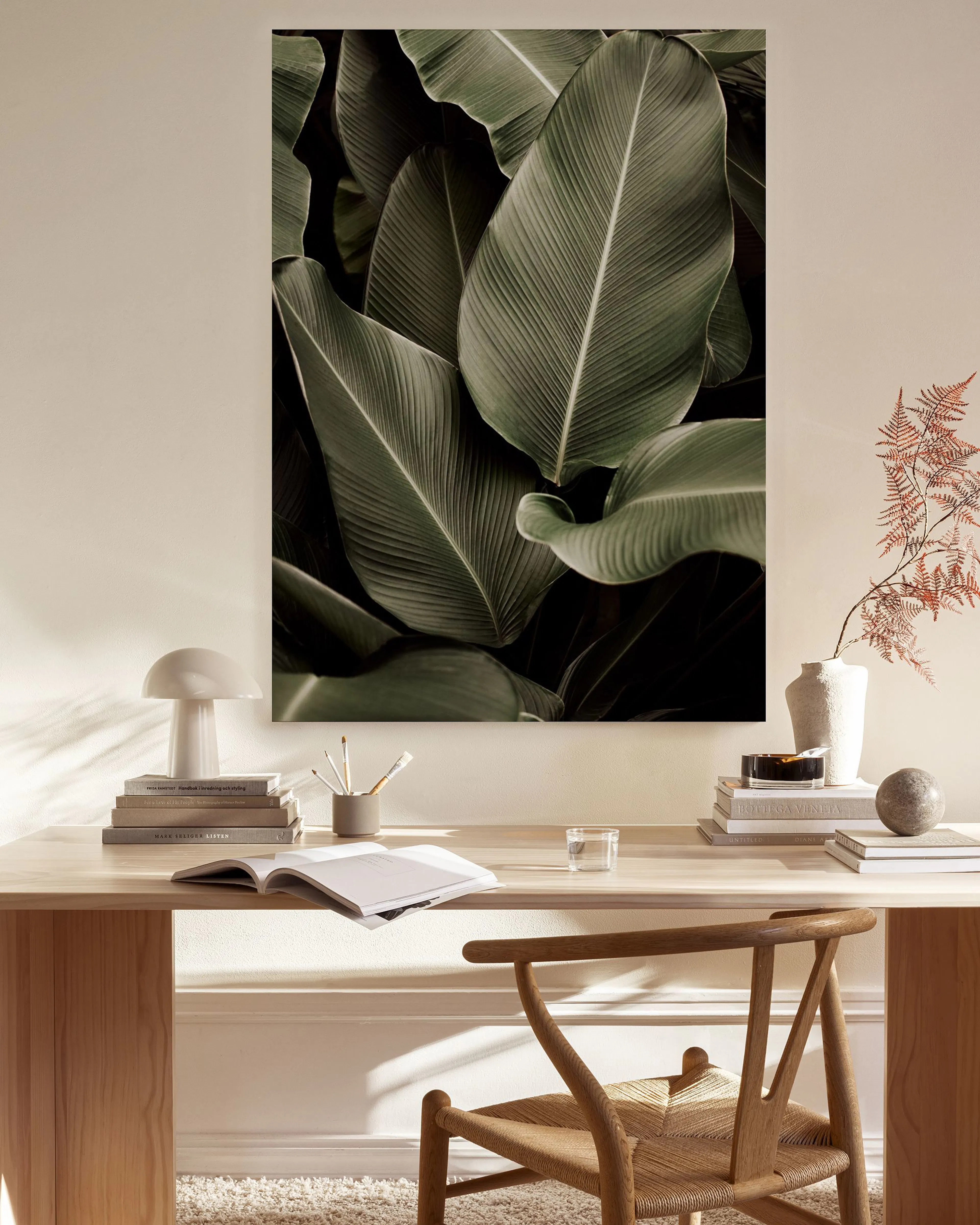 A canvas print of large green banana leaves on a light wall in a modern living room with a wooden chair and coffee table.